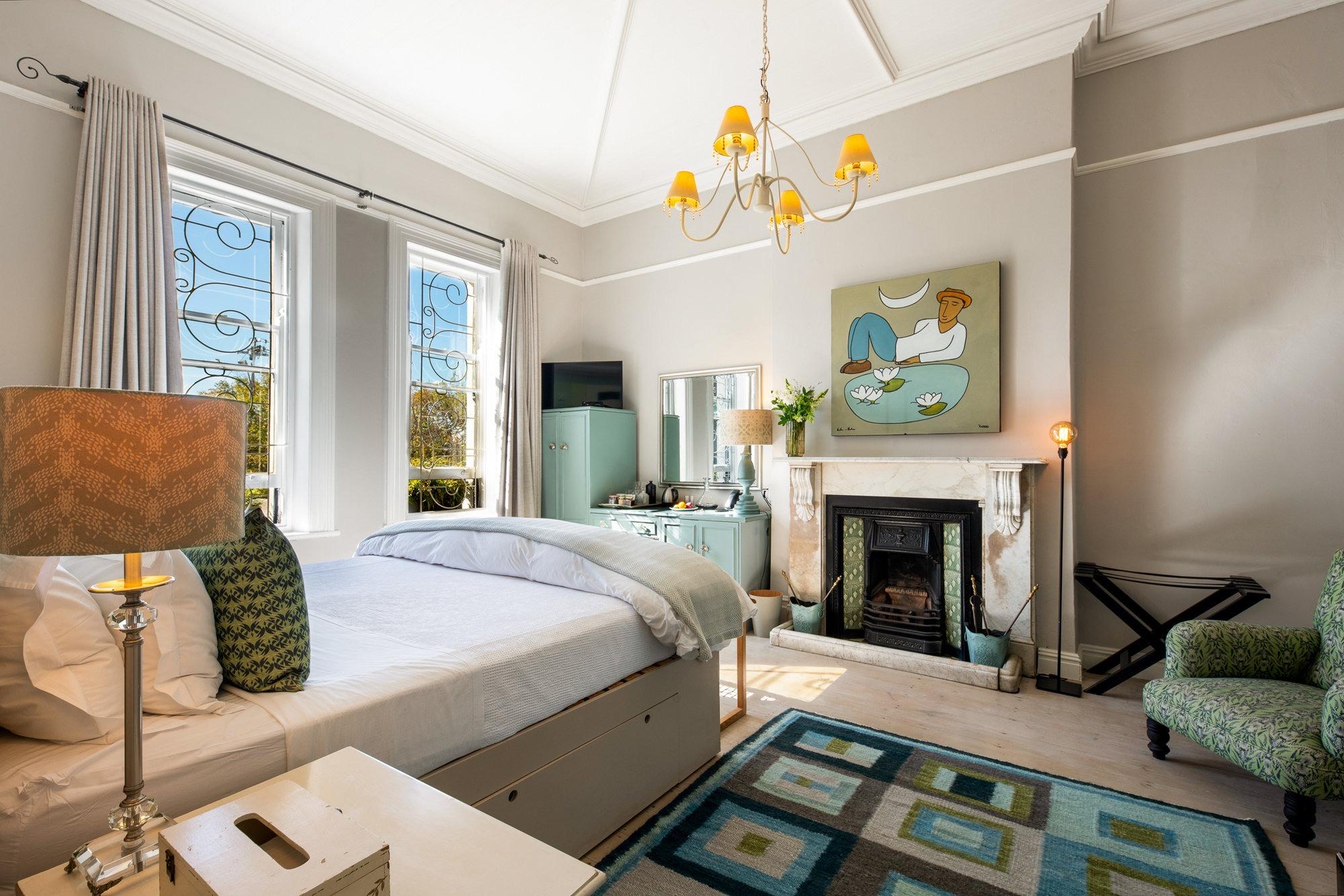 a bedroom with a white marble fireplace, a colourful painting above the mantel, and barred windows looking toward a mountain