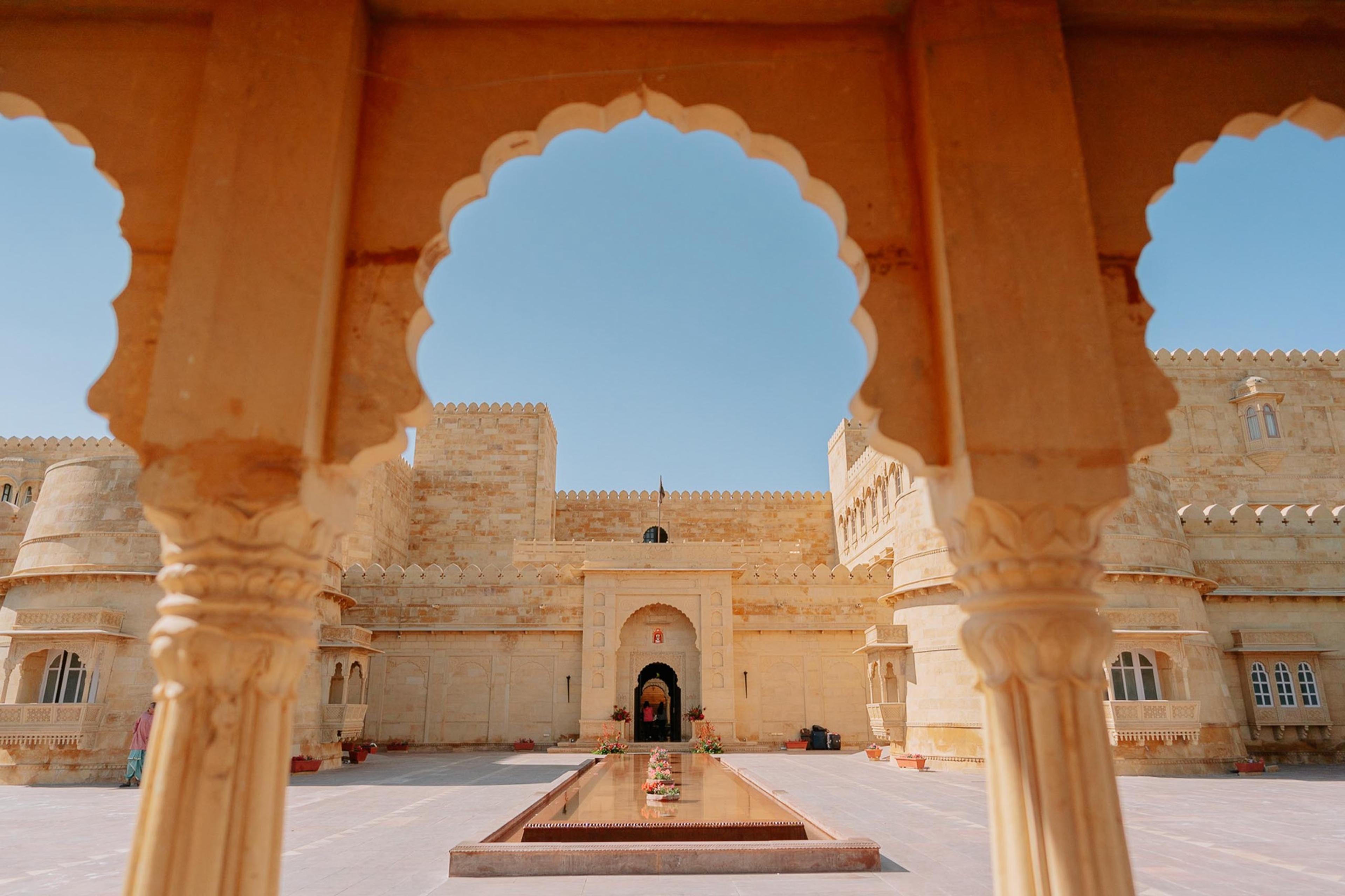a scalloped stone archway framing a sandstone courtyard with a narrow water channel leading to the palace entrance