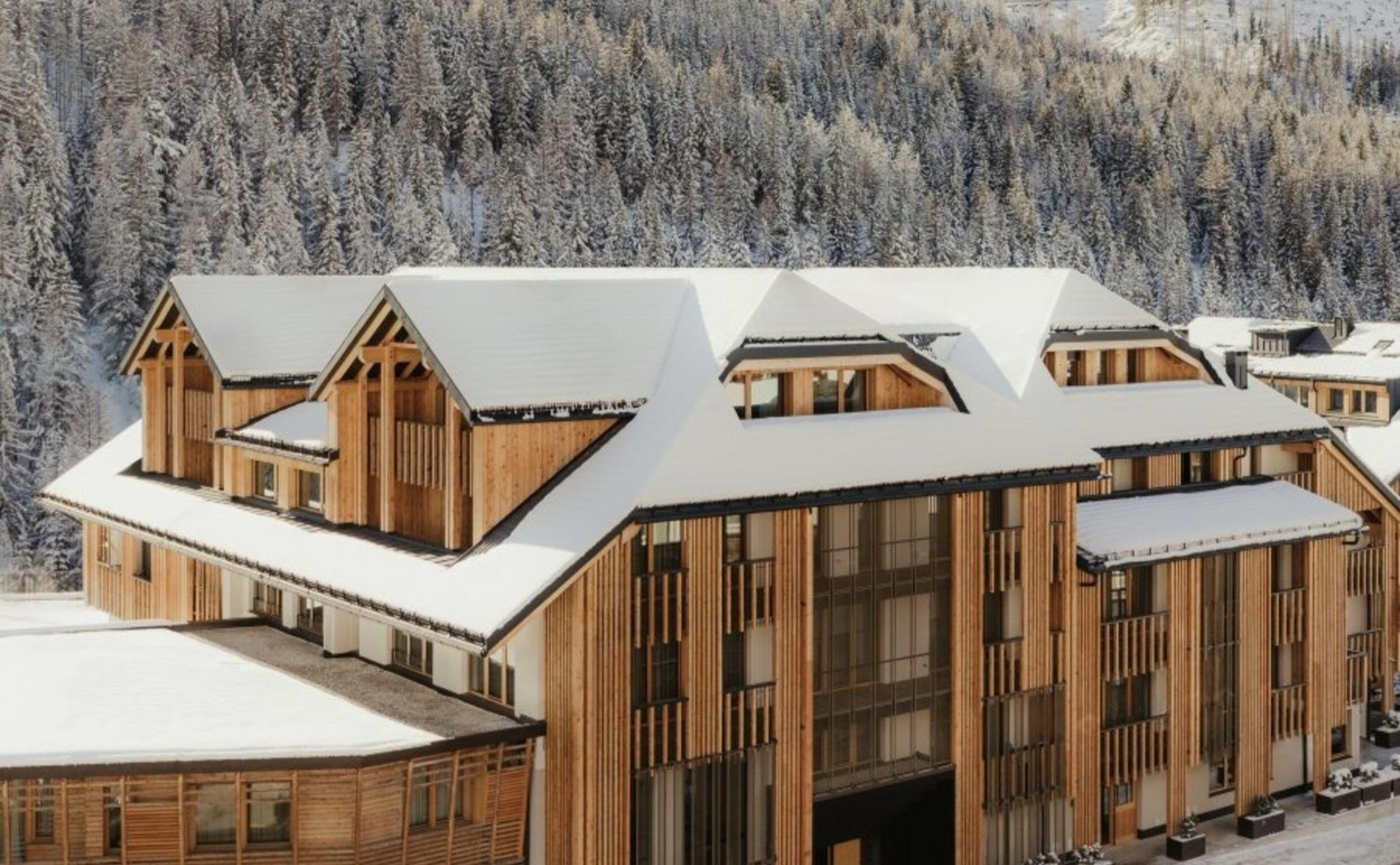 Snow lying on the hotel's timber roofs and balconies, with snow-covered pines on the slope behind.
