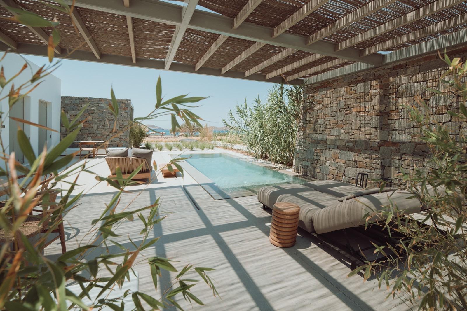 A covered terrace with a reed roof, daybeds and a small plunge pool, looking out past a stone wall to the sea.