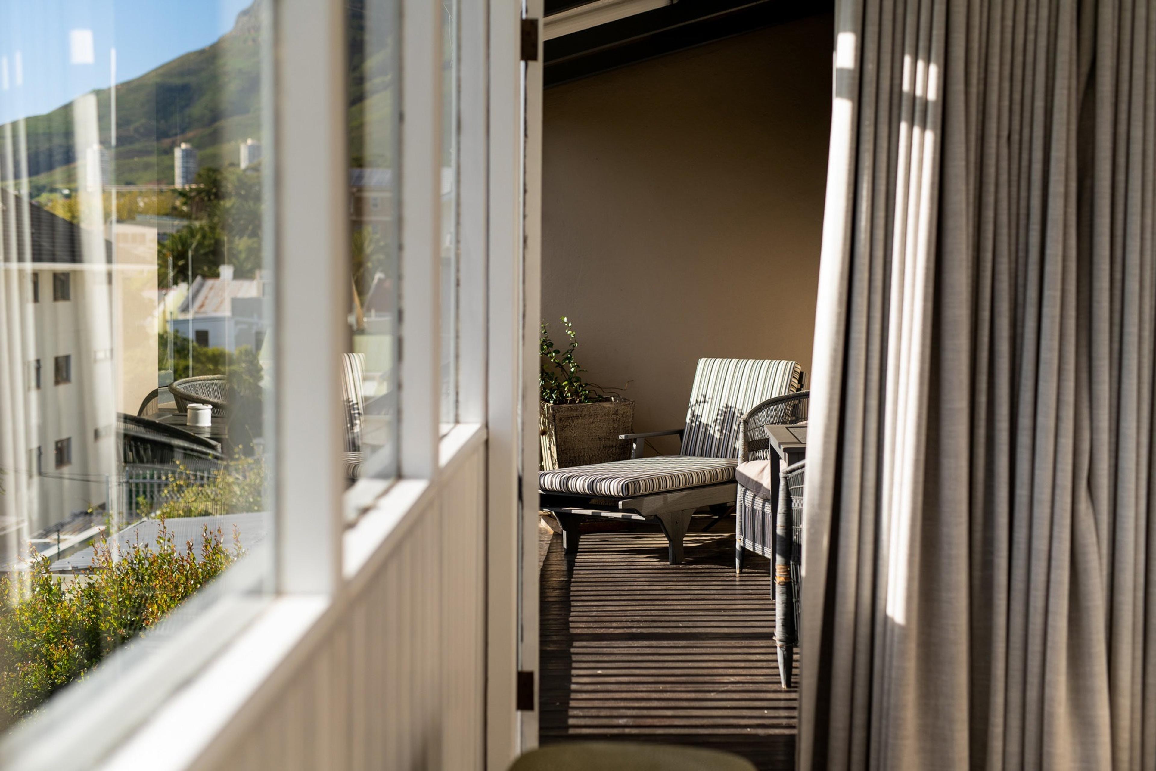 a narrow balcony with two striped lounge chairs seen through an open door, with a tree-covered mountain and city buildings beyond
