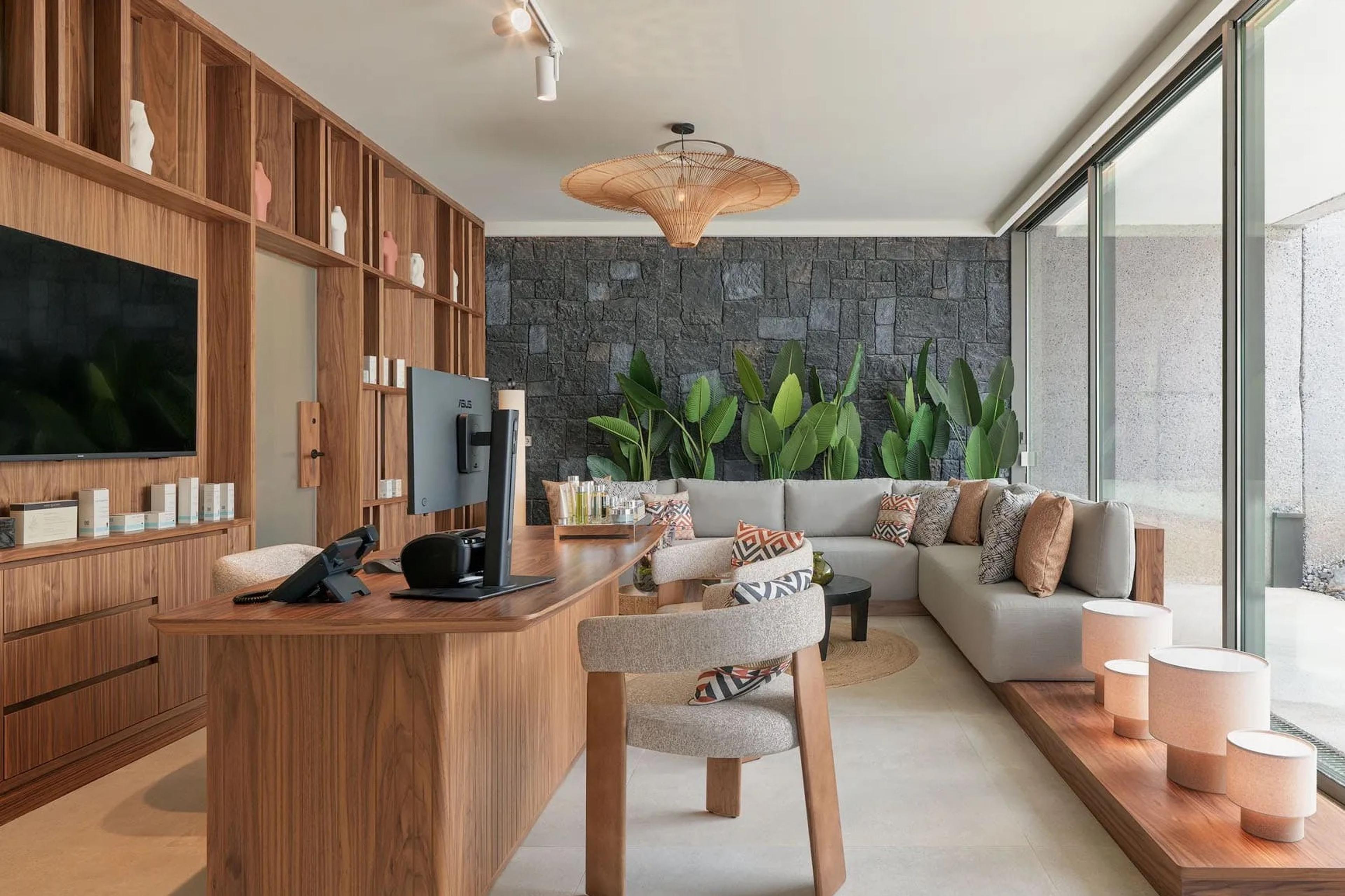 A lounge area with a grey sectional sofa, patterned cushions, a wall of dark stone, and a wooden desk with a monitor.