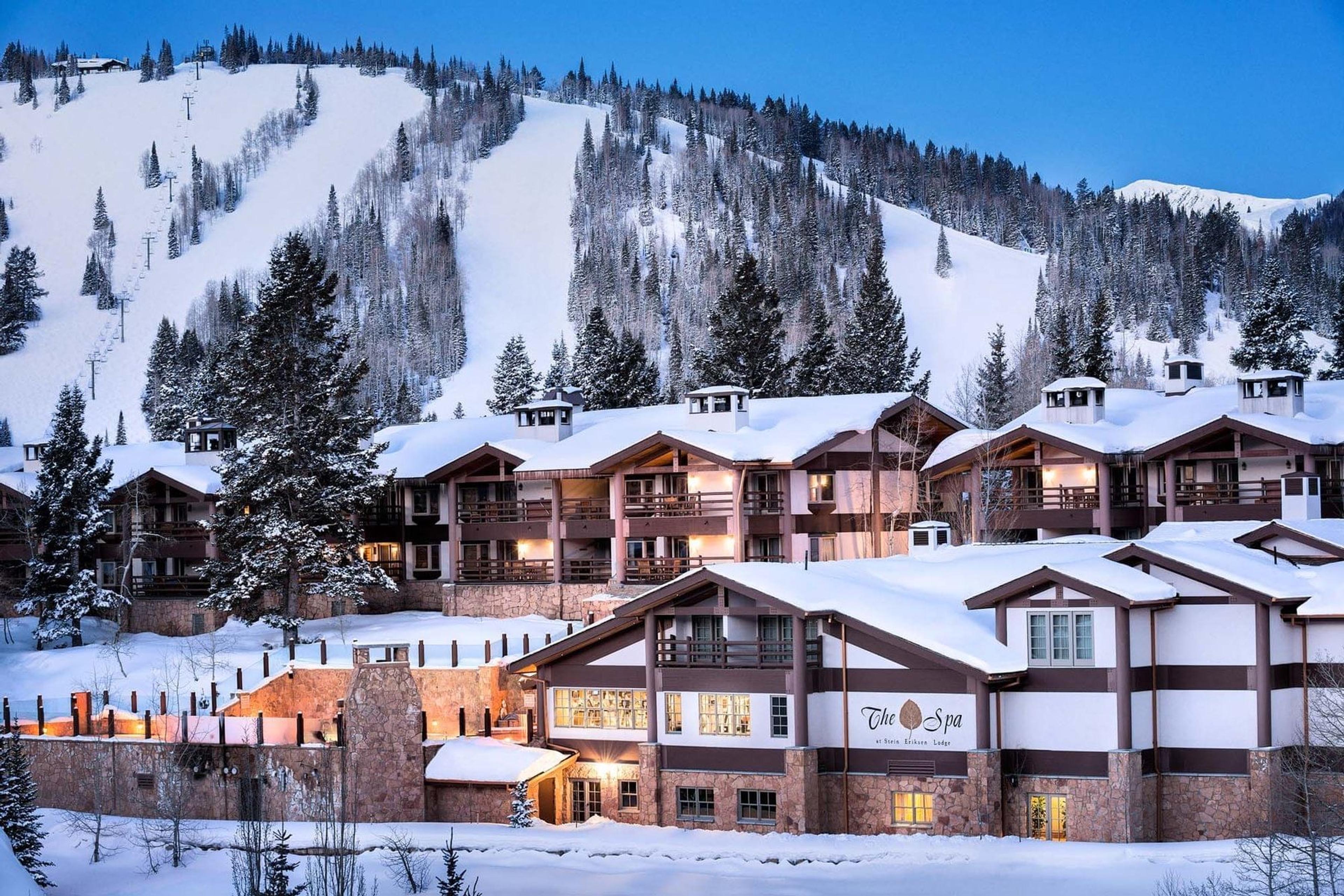 a timber lodge building lit up at dusk in the snow, with The Spa signage on one wing and a floodlit ski run rising behind it
