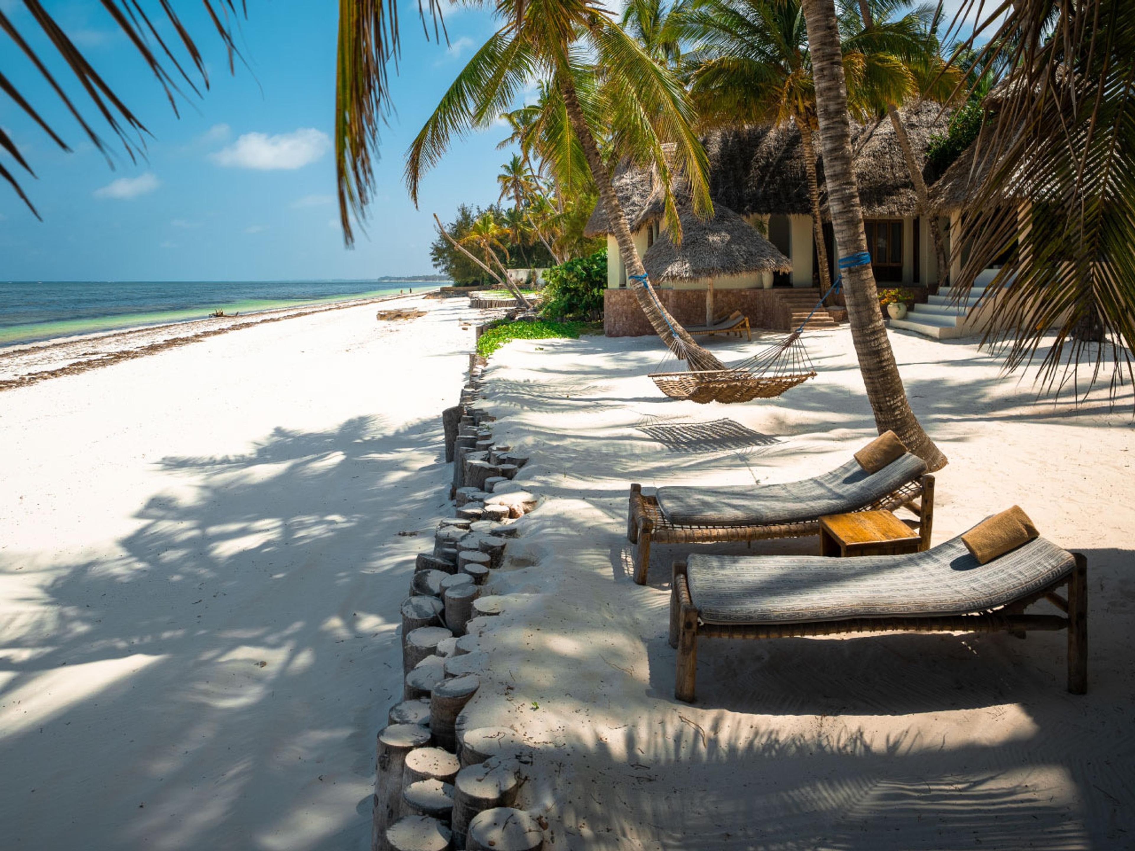 Loungers on white sand under palms, with the Indian Ocean beyond
