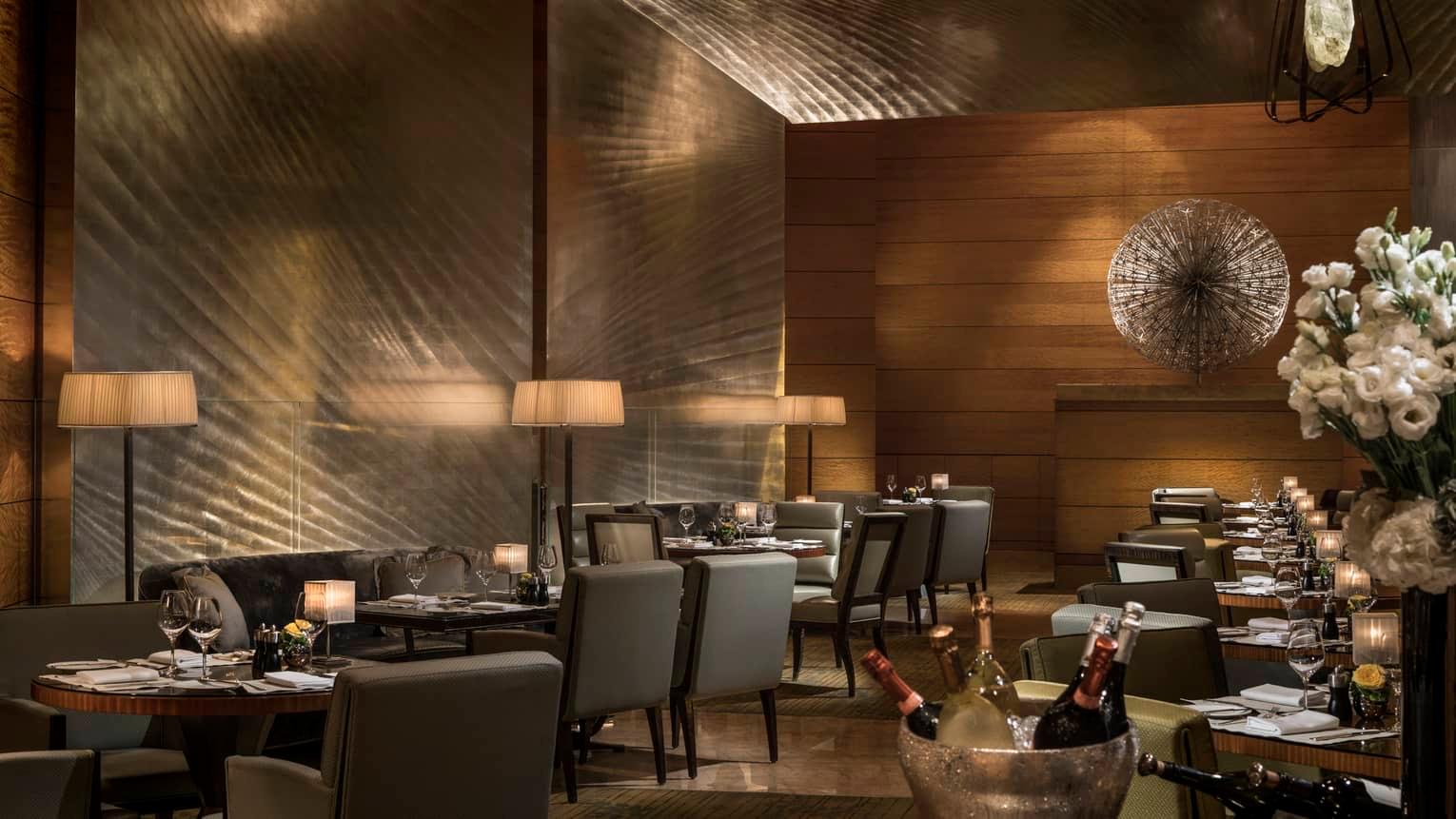 A dining room lined in burnished metal and wood, with tables laid for dinner