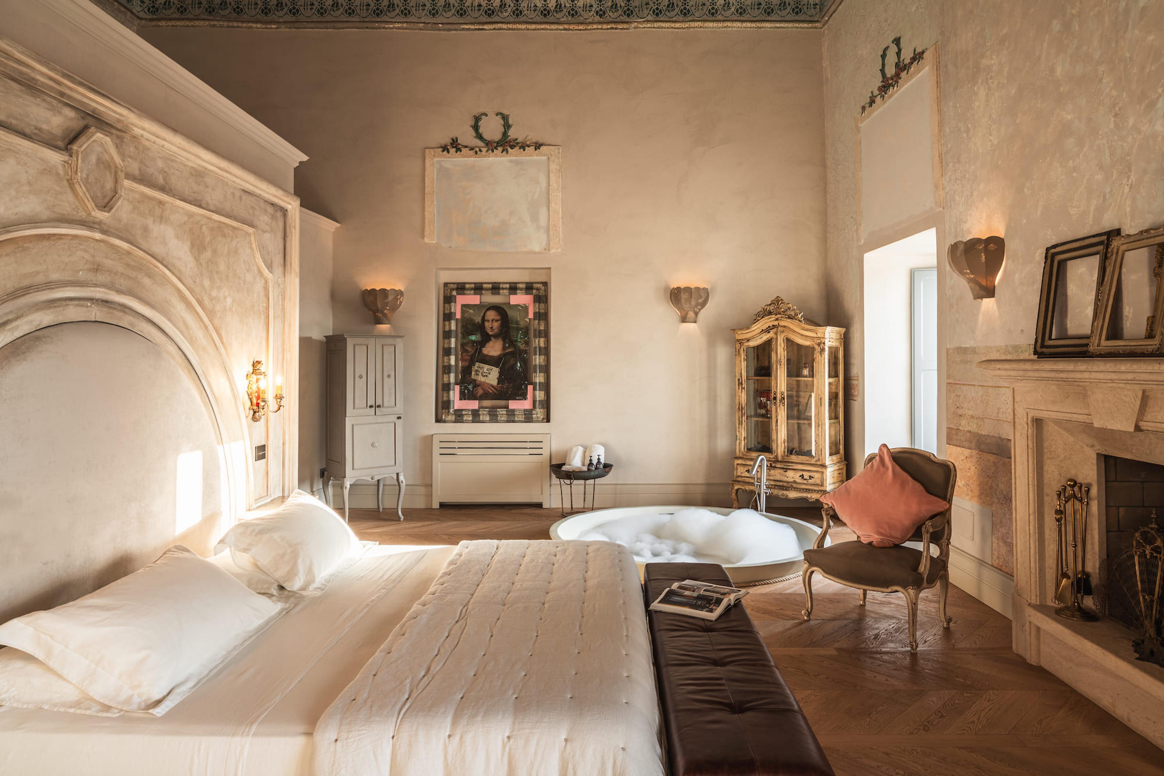A canopied suite bedroom with an arched stone headboard, a round bubble-filled bathtub beside the bed, and a brightly framed pop-art print of the Mona Lisa on the wall.