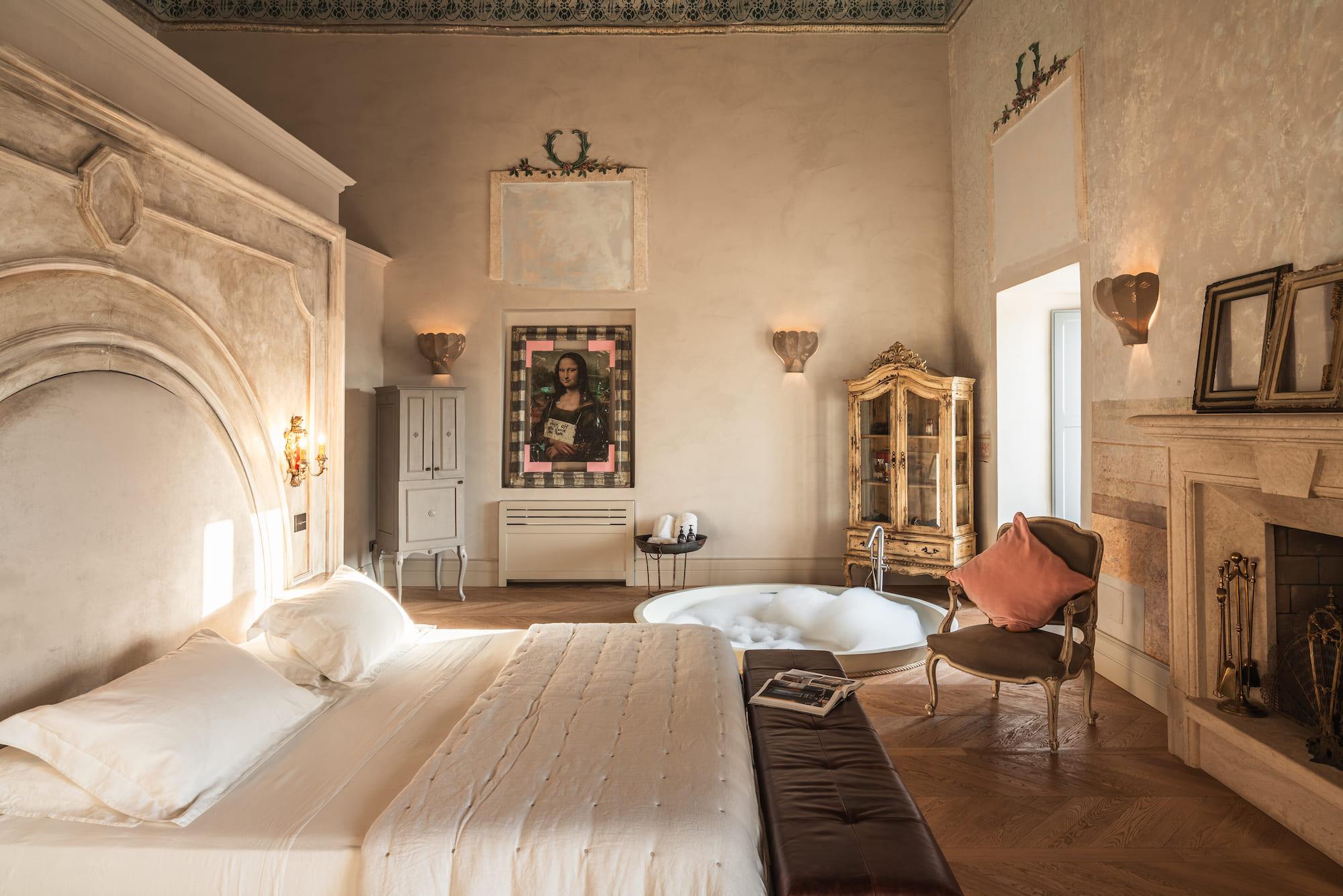 A canopied suite bedroom with an arched stone headboard, a round bubble-filled bathtub beside the bed, and a brightly framed pop-art print of the Mona Lisa on the wall.