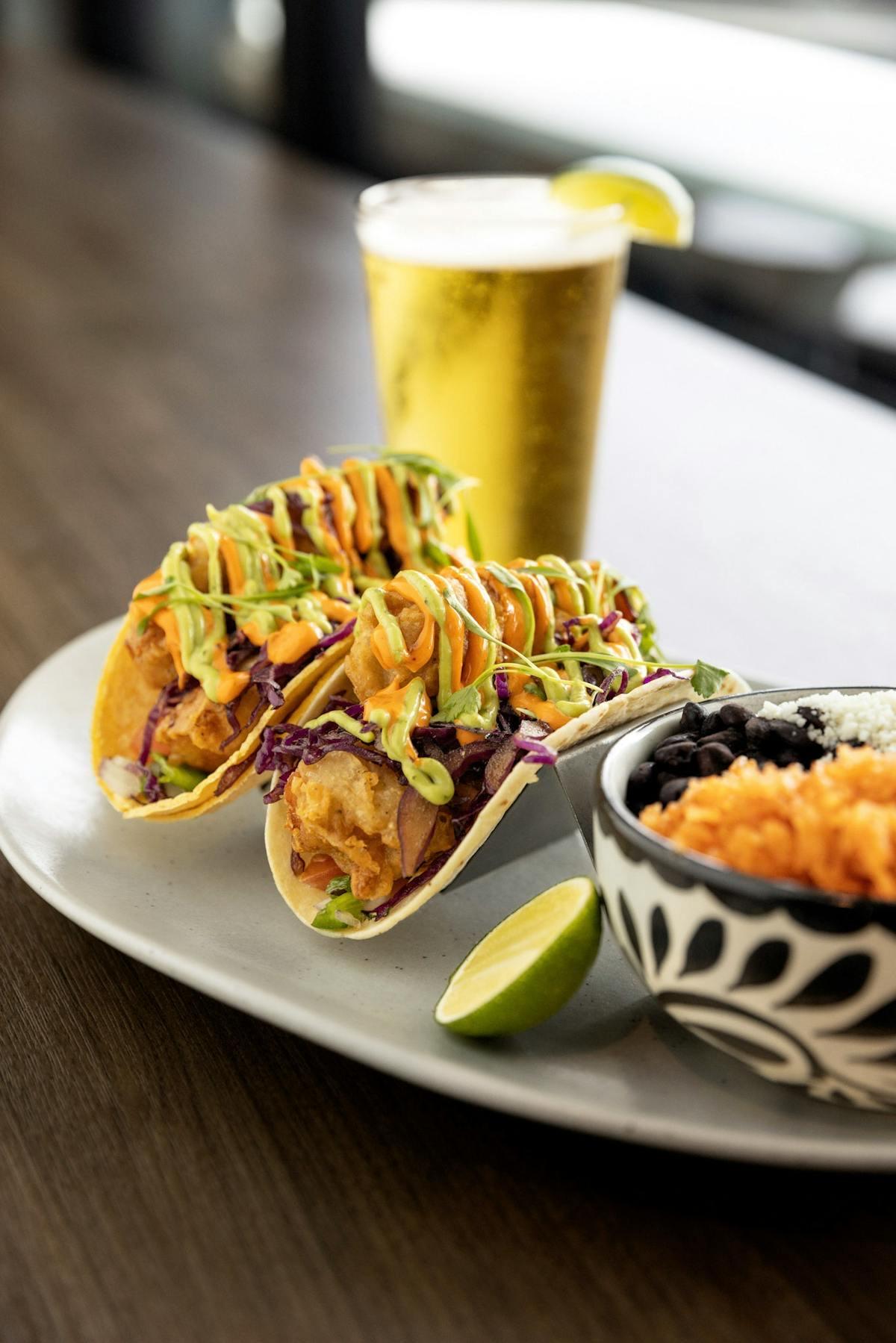 Tacos topped with slaw and lime, beside a dish of rice