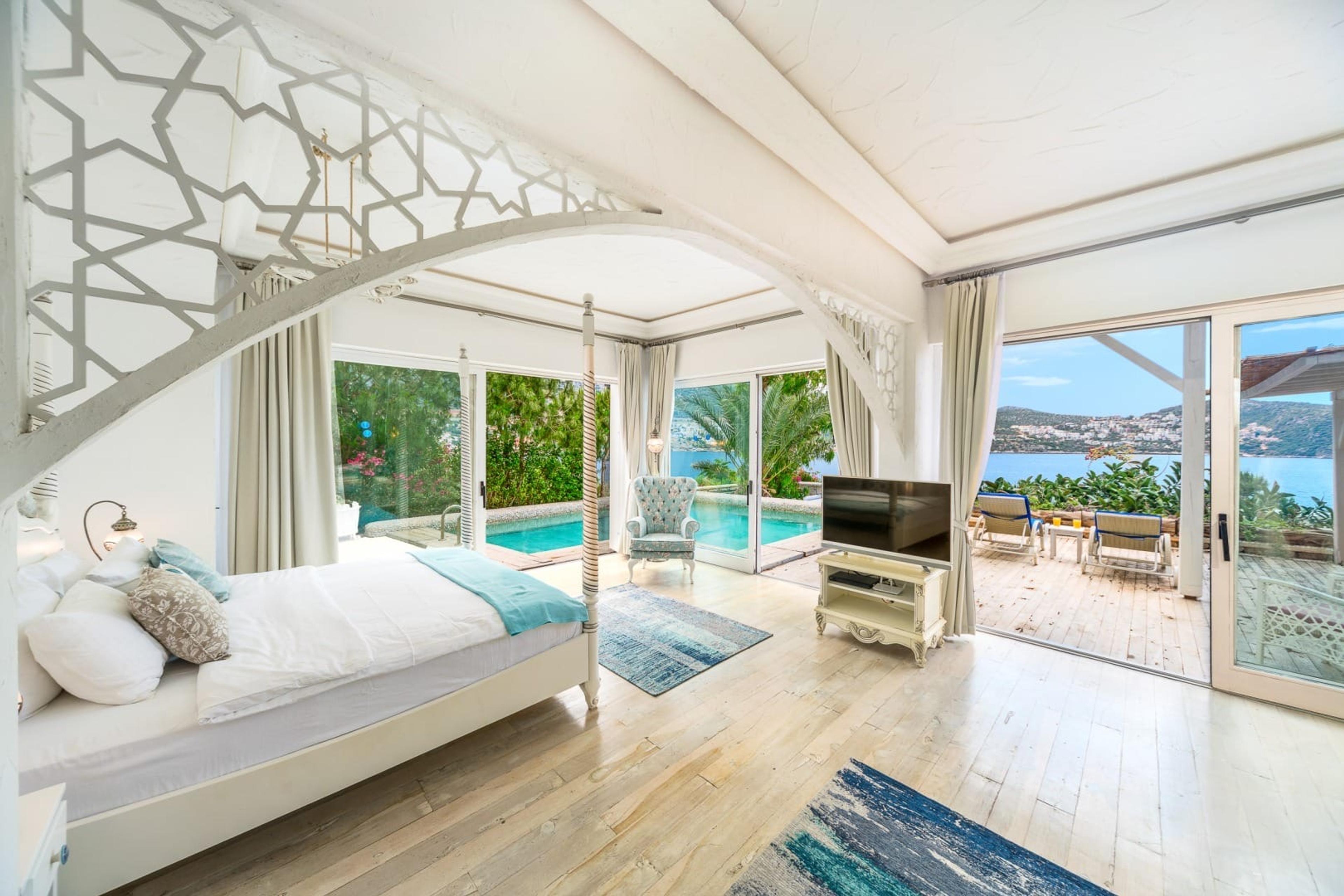 A bedroom with a carved white archway over a four-poster bed, glass doors folded open onto a private pool and the sea beyond.