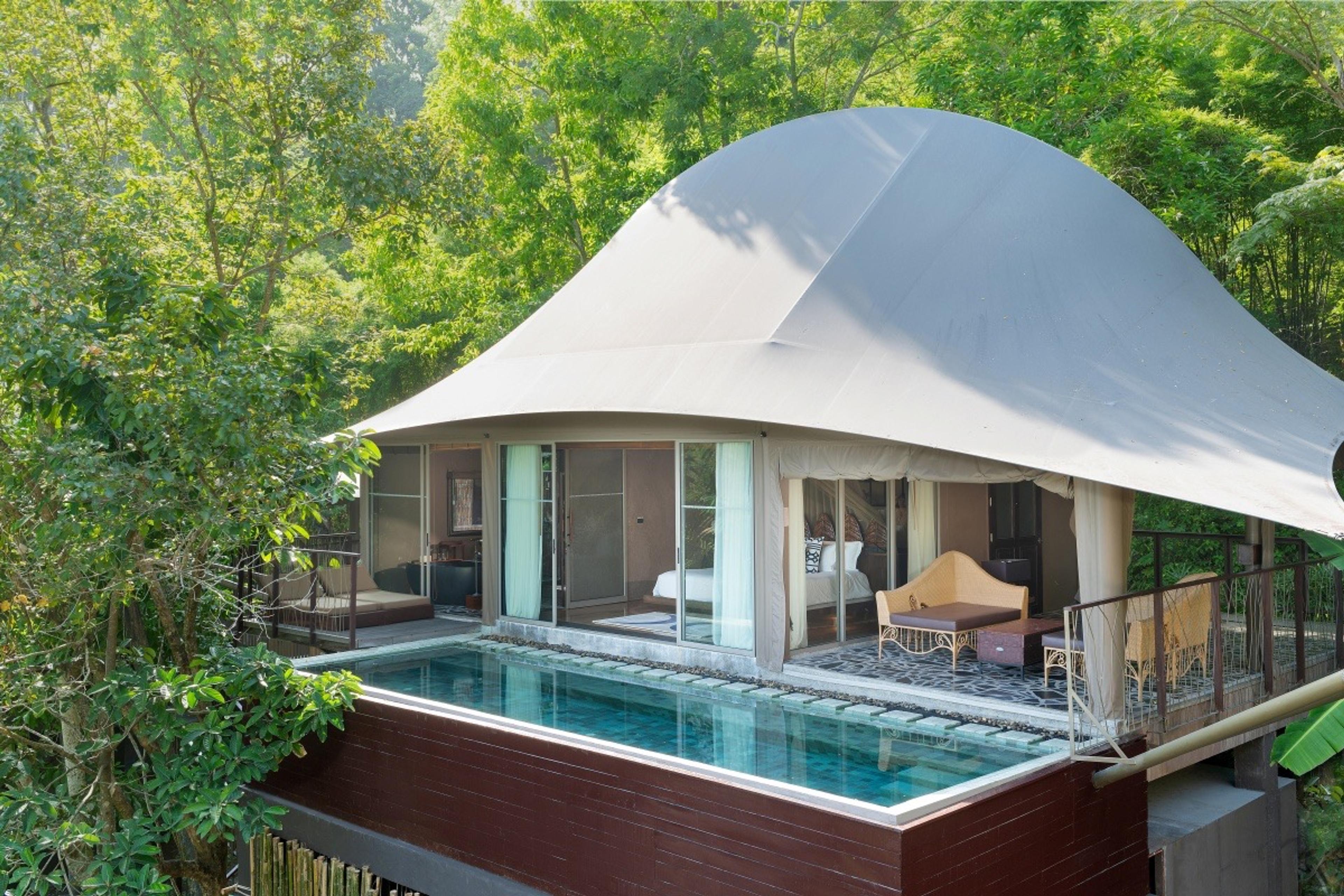 A tented villa with its own plunge pool, daybeds and lounge seating on a deck surrounded by trees.