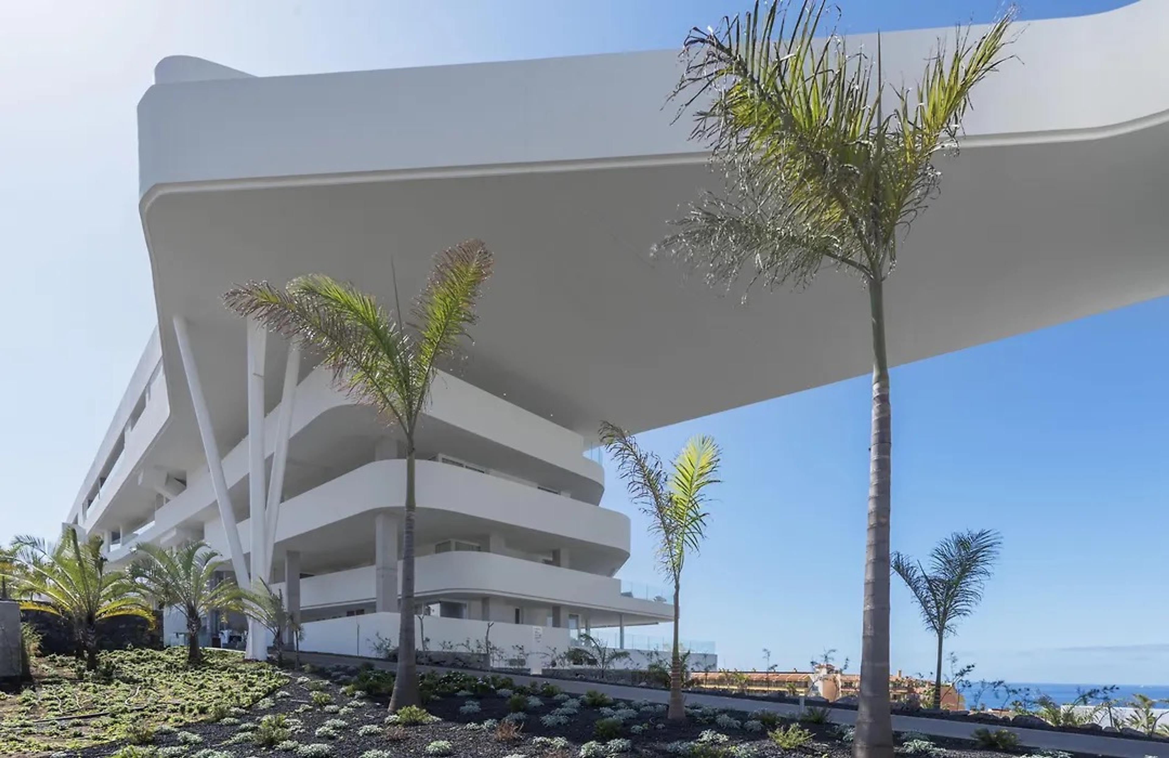 The hotel's white, sculpted curving floors and a canopy above palms, against a blue sky