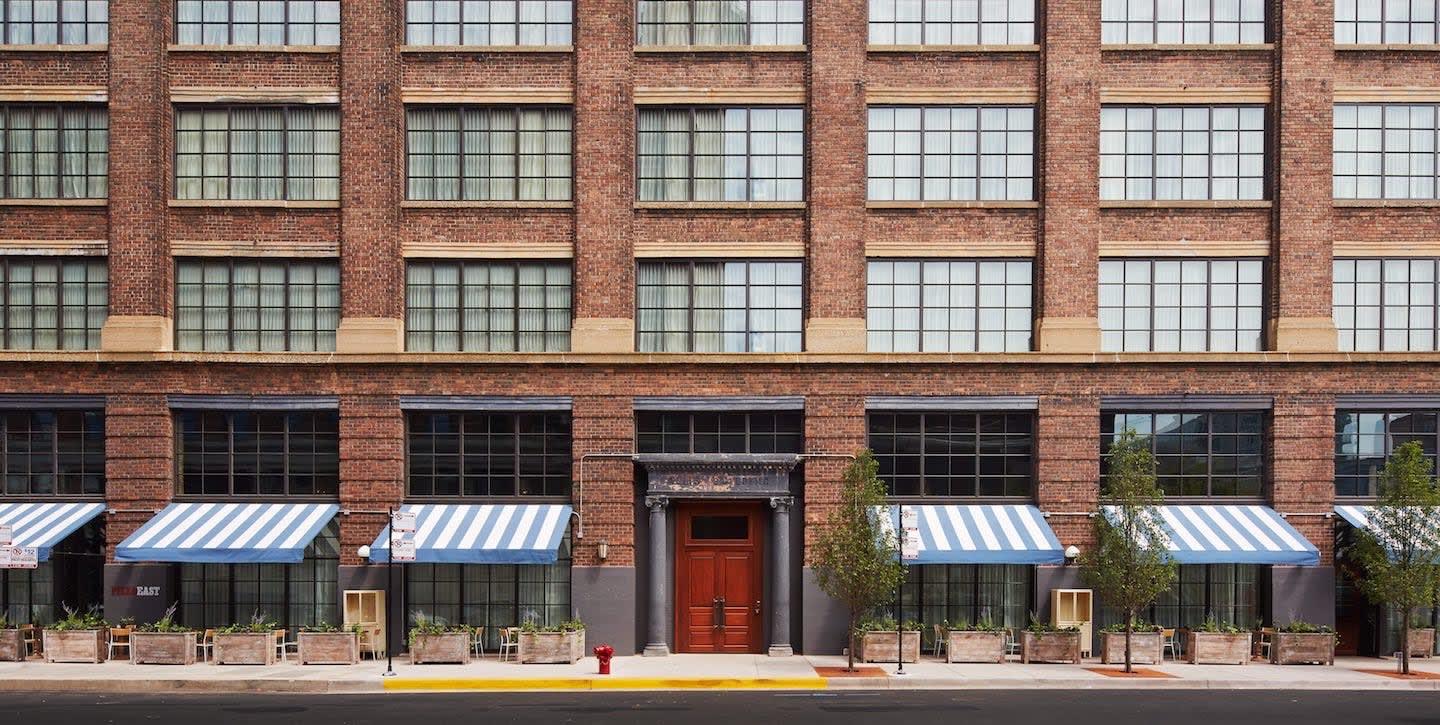 A six-storey brick warehouse building with a row of blue and white striped awnings, large arched windows, and a central wooden double door at street level.