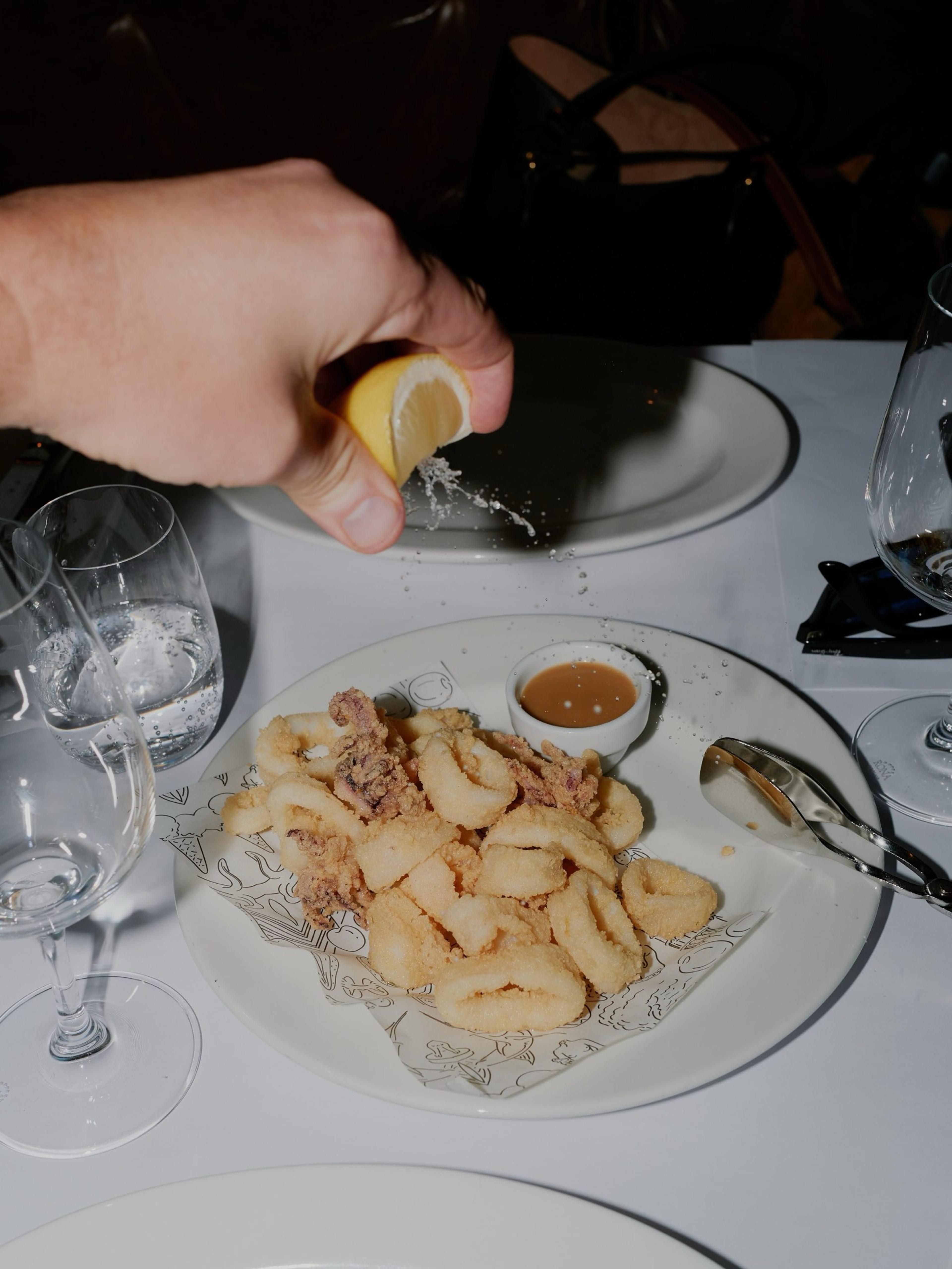 A hand grating cheese over a plate of pasta on a white tablecloth