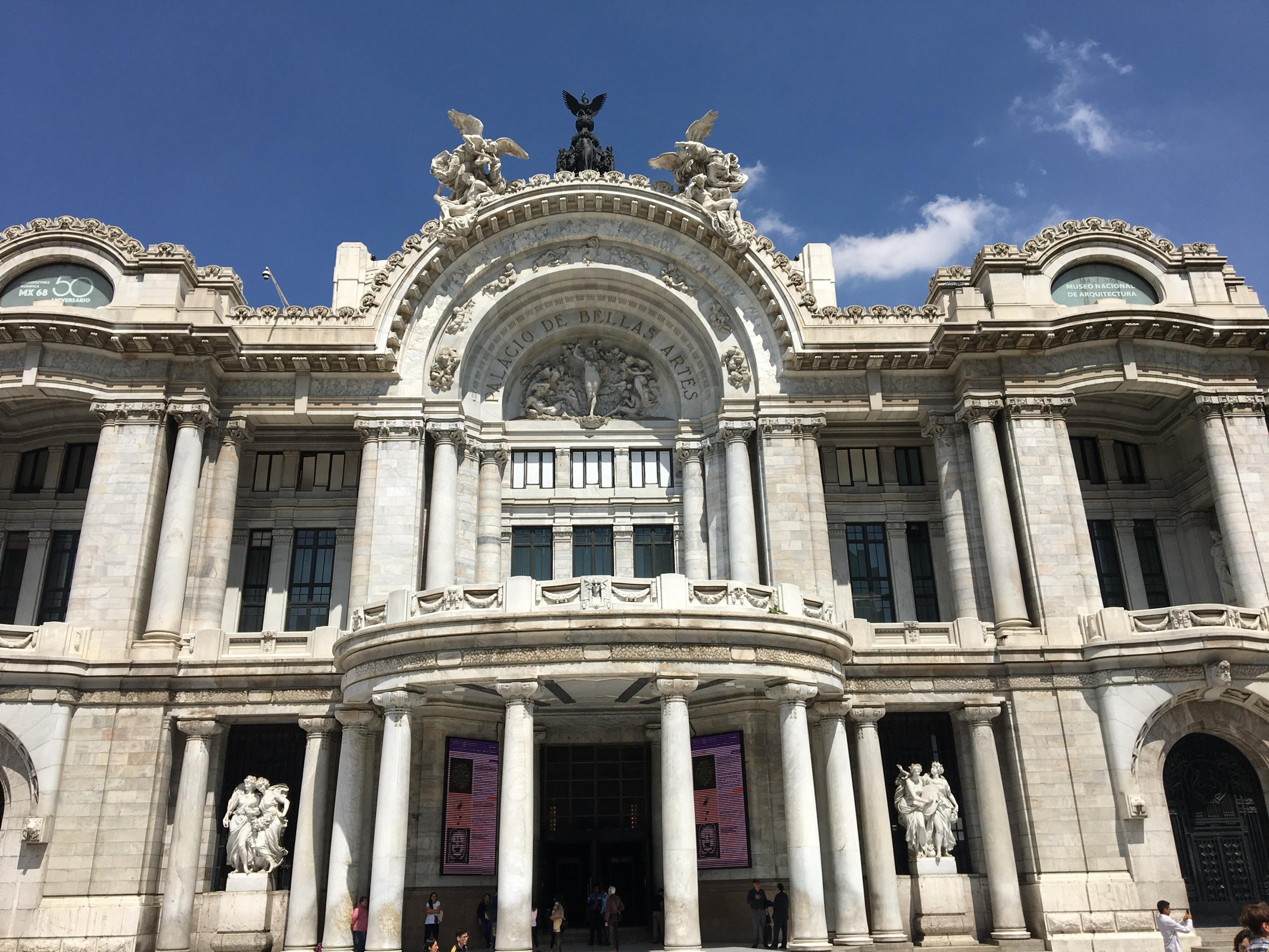 The white marble facade of the Palacio de Bellas Artes in Mexico City, its ornate domes and sculpted arches under a bright blue sky
