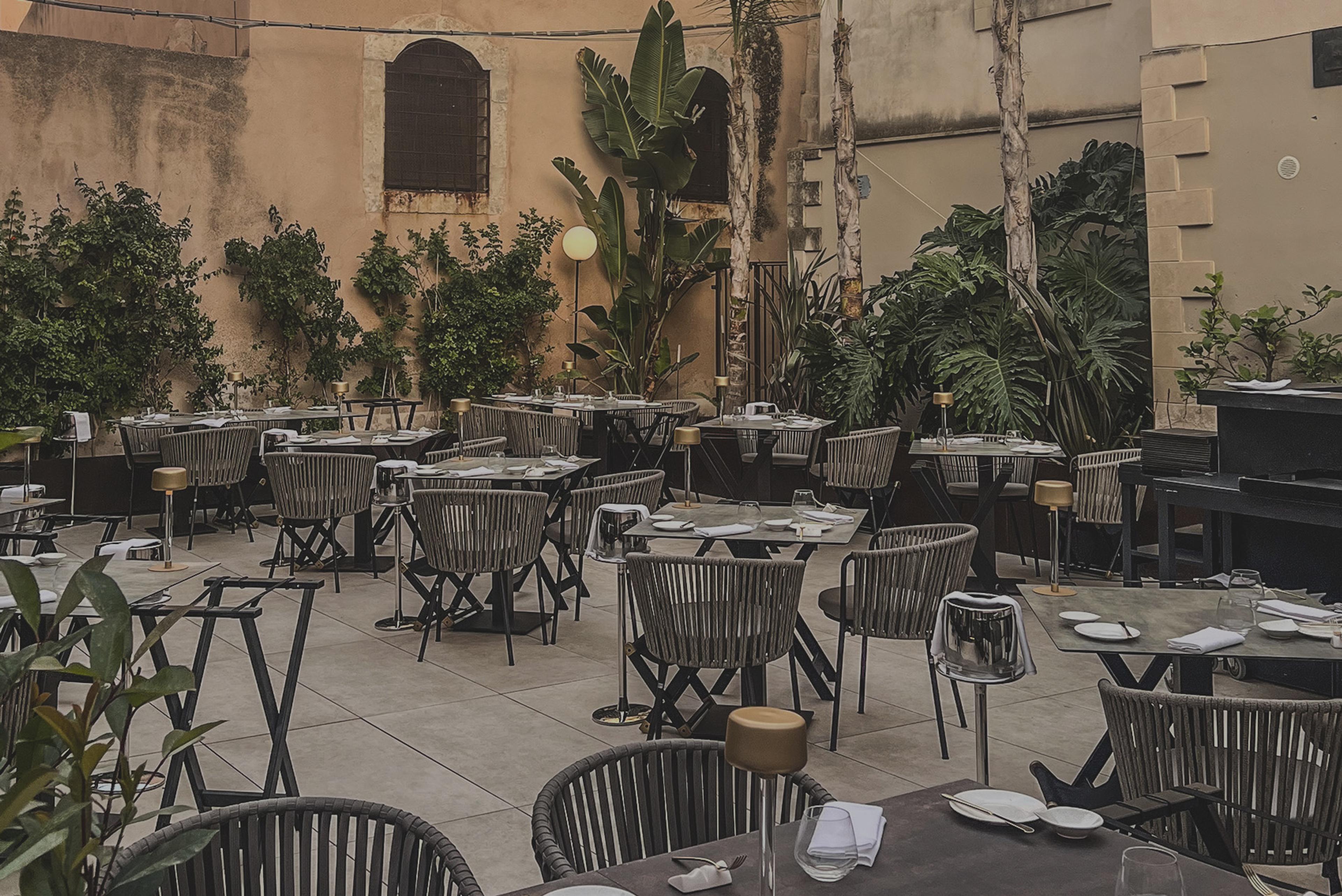 Tables set among potted palms in the stone courtyard of Cortile Spirito Santo