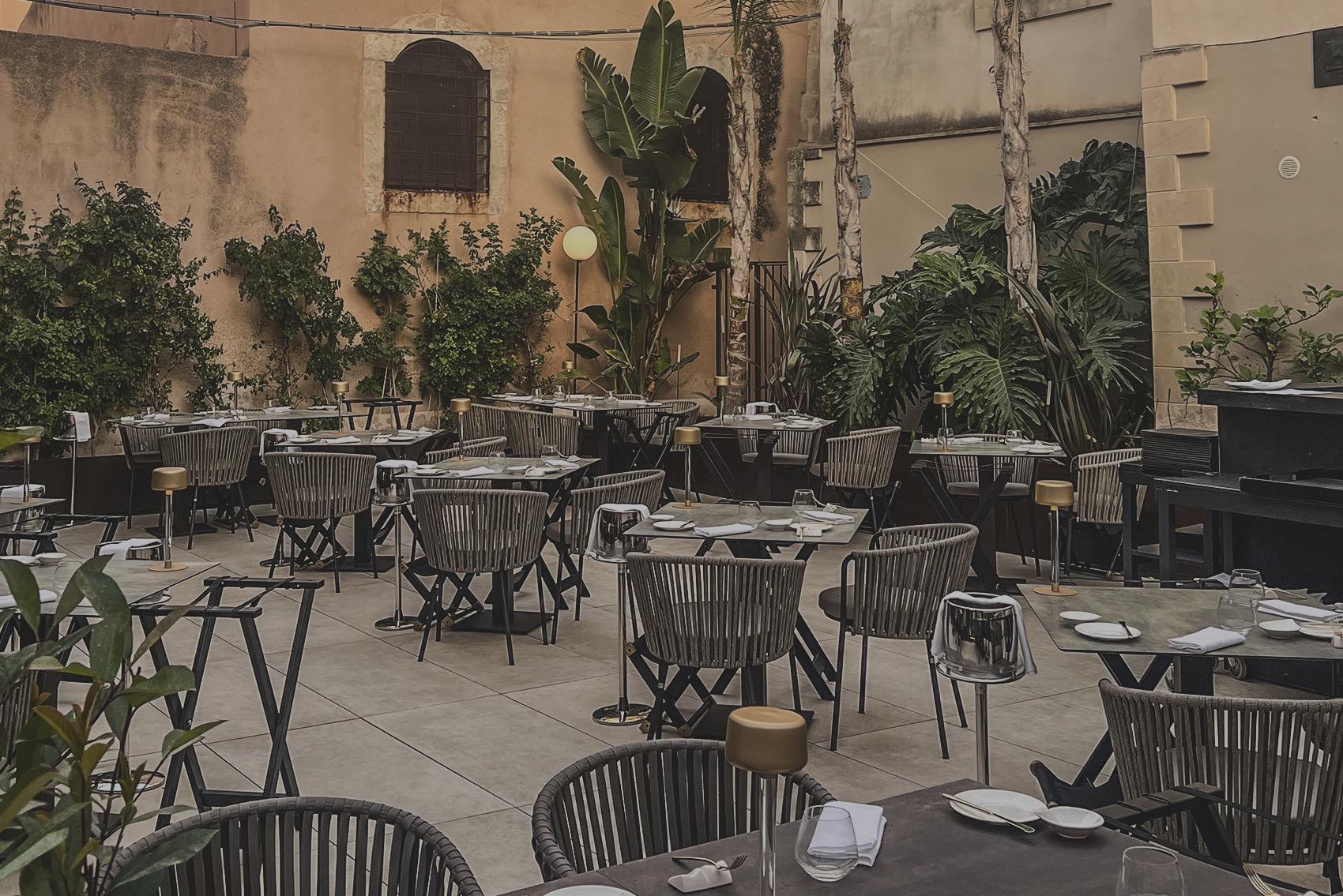 Tables set among potted palms in the stone courtyard of Cortile Spirito Santo