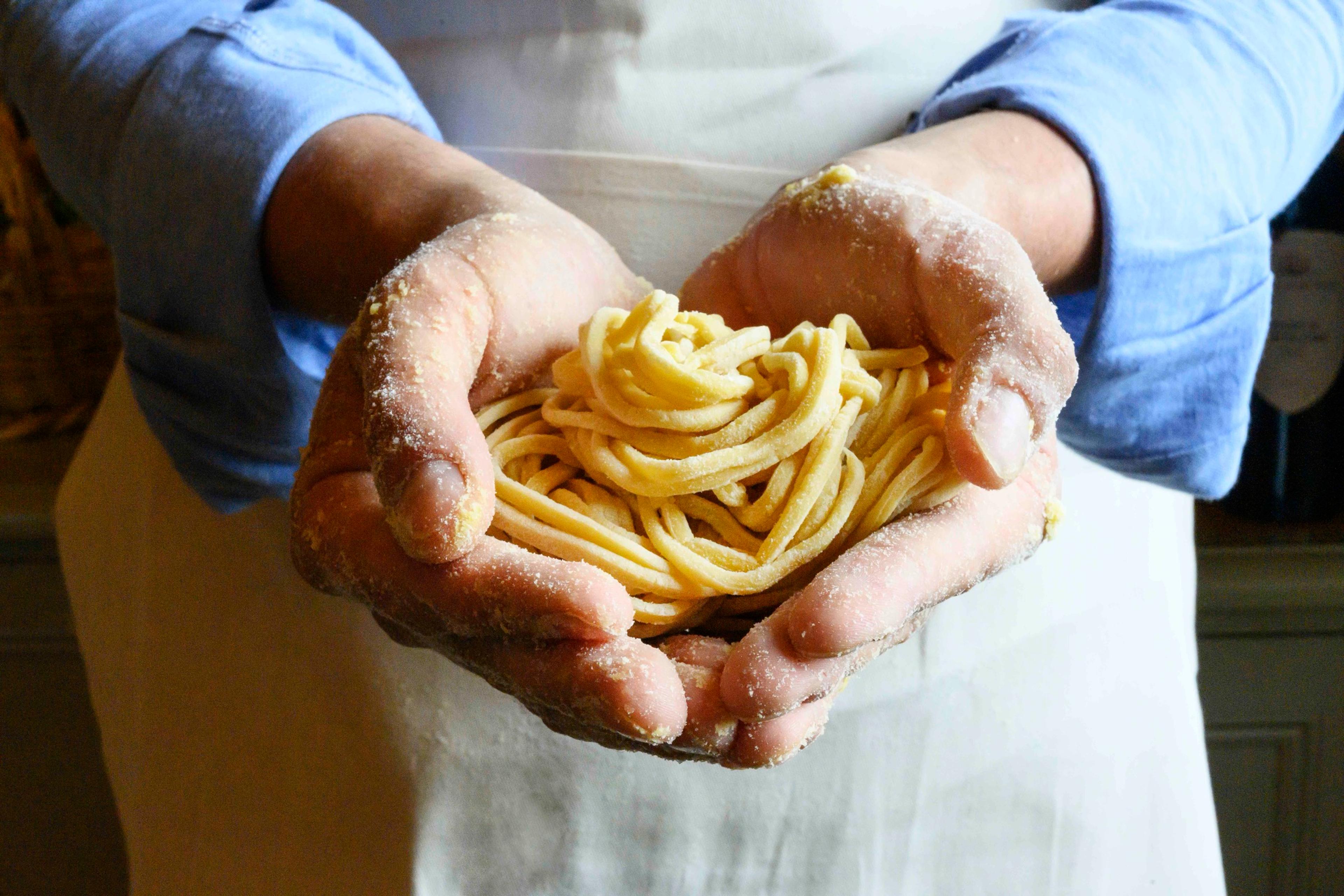Two cupped hands holding a nest of fresh pasta.