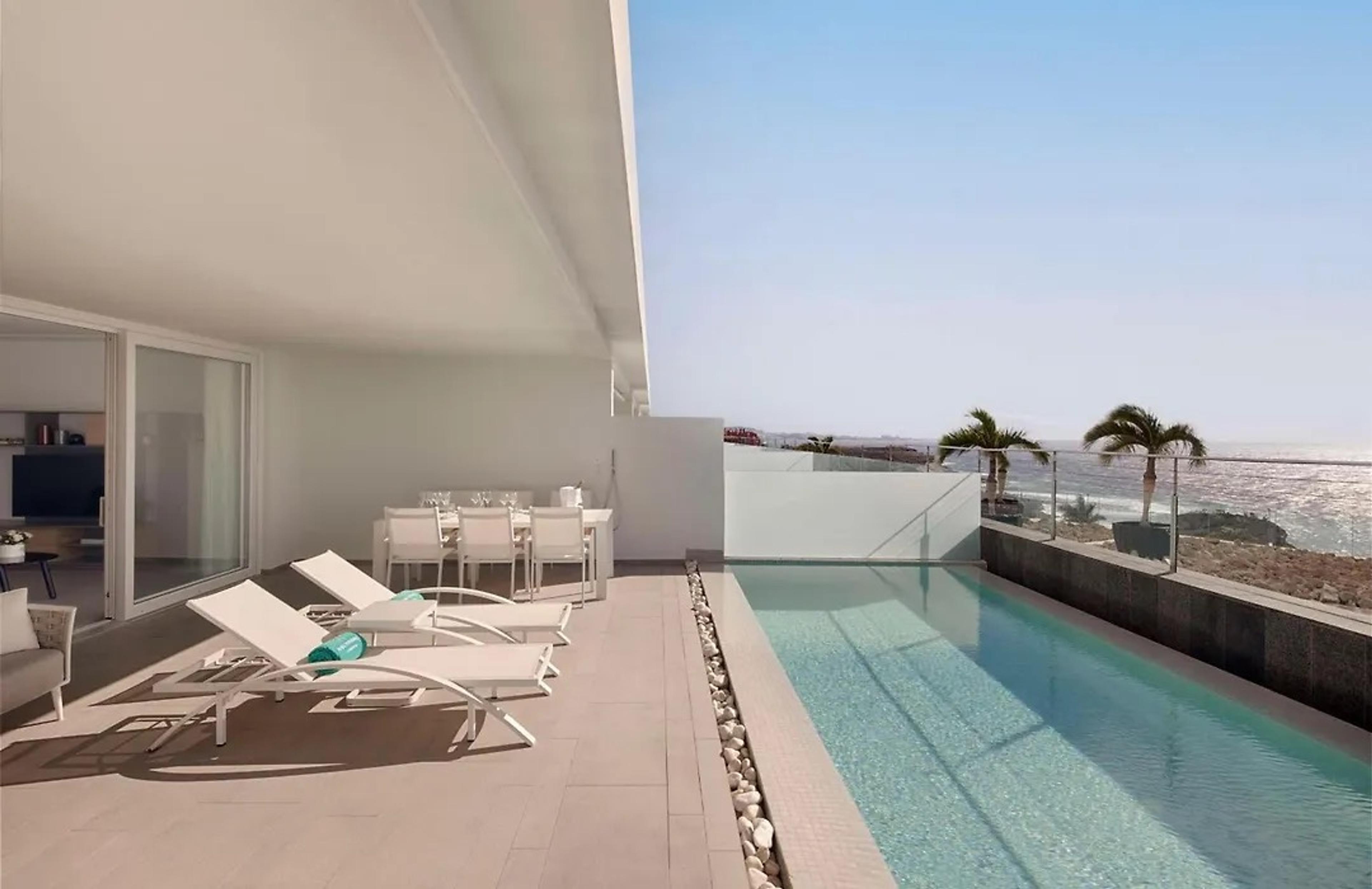 A suite's private terrace with a long pool, sun loungers and an outdoor dining table, looking out to sea