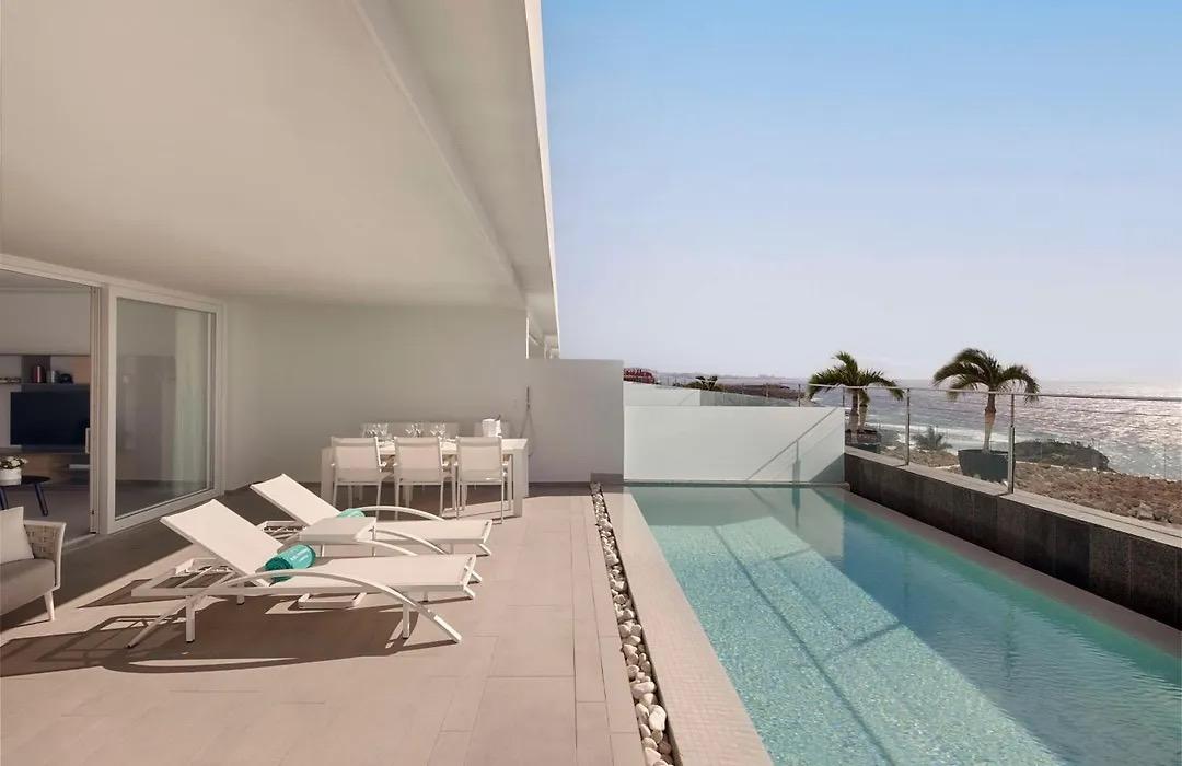 A suite's private terrace with a long pool, sun loungers and an outdoor dining table, looking out to sea
