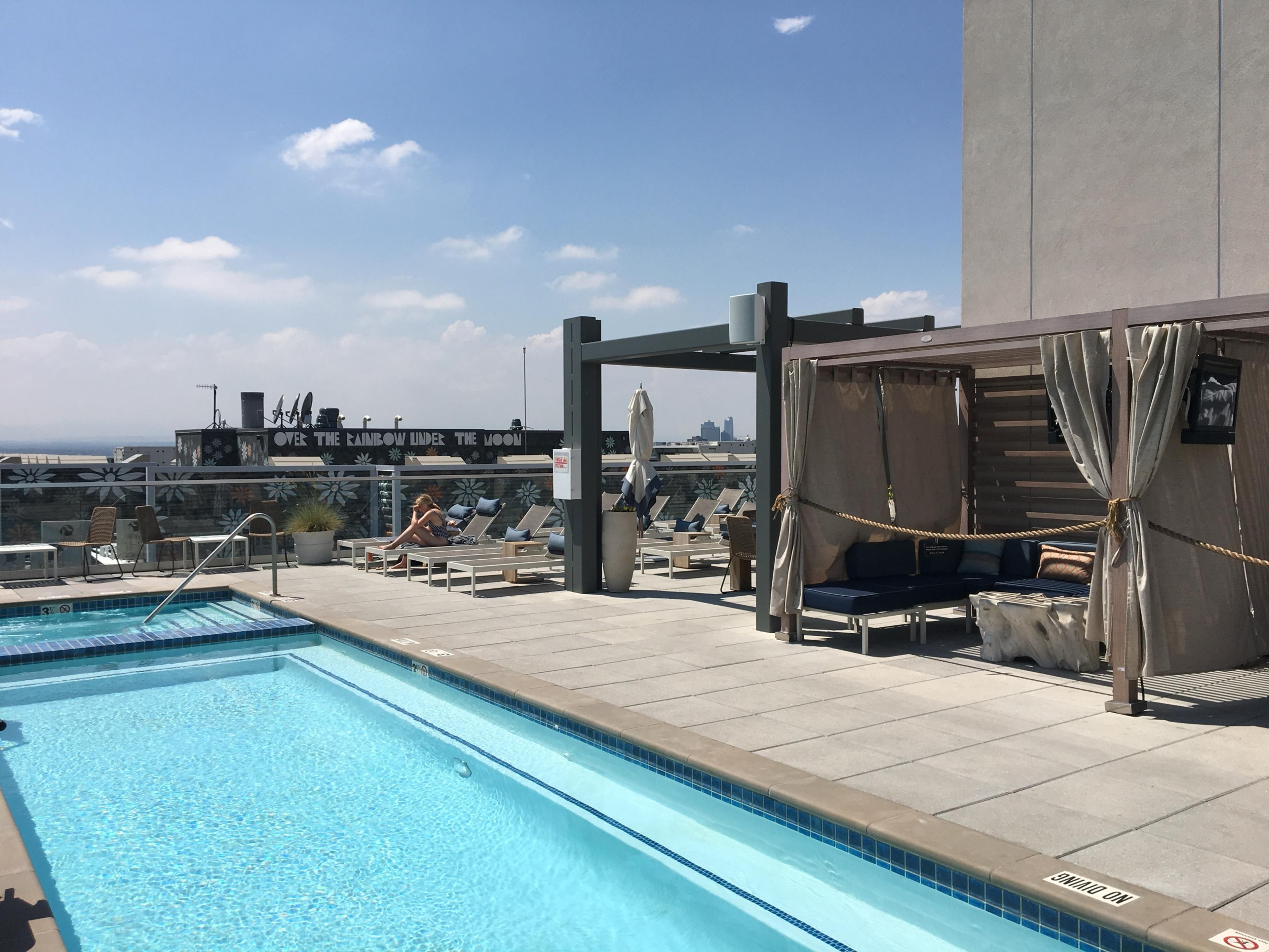 A rooftop pool with loungers and curtained cabanas, with the city spreading out beyond