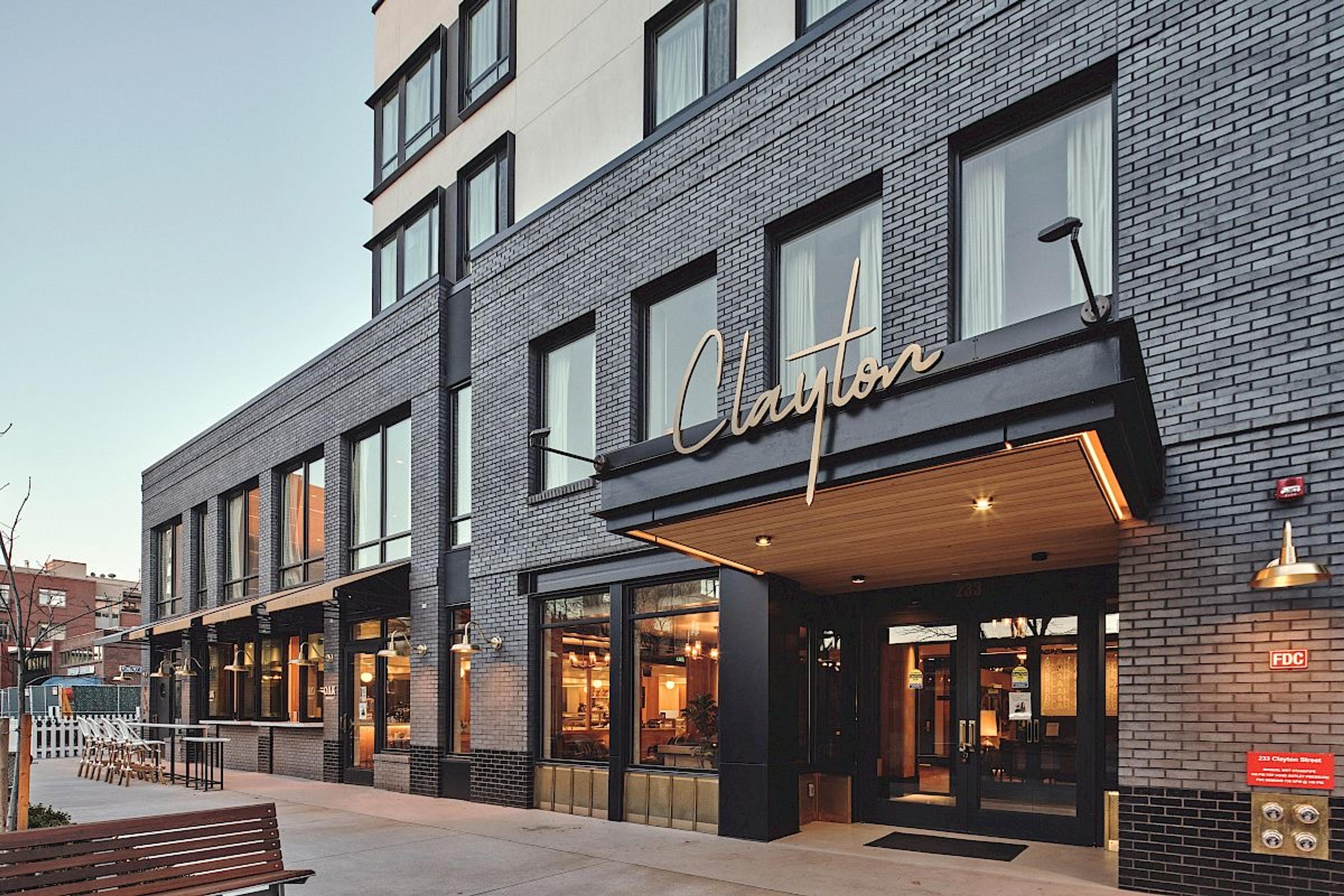 The hotel's dark brick front at dusk, its name in gold script above a lit wooden canopy over the entrance