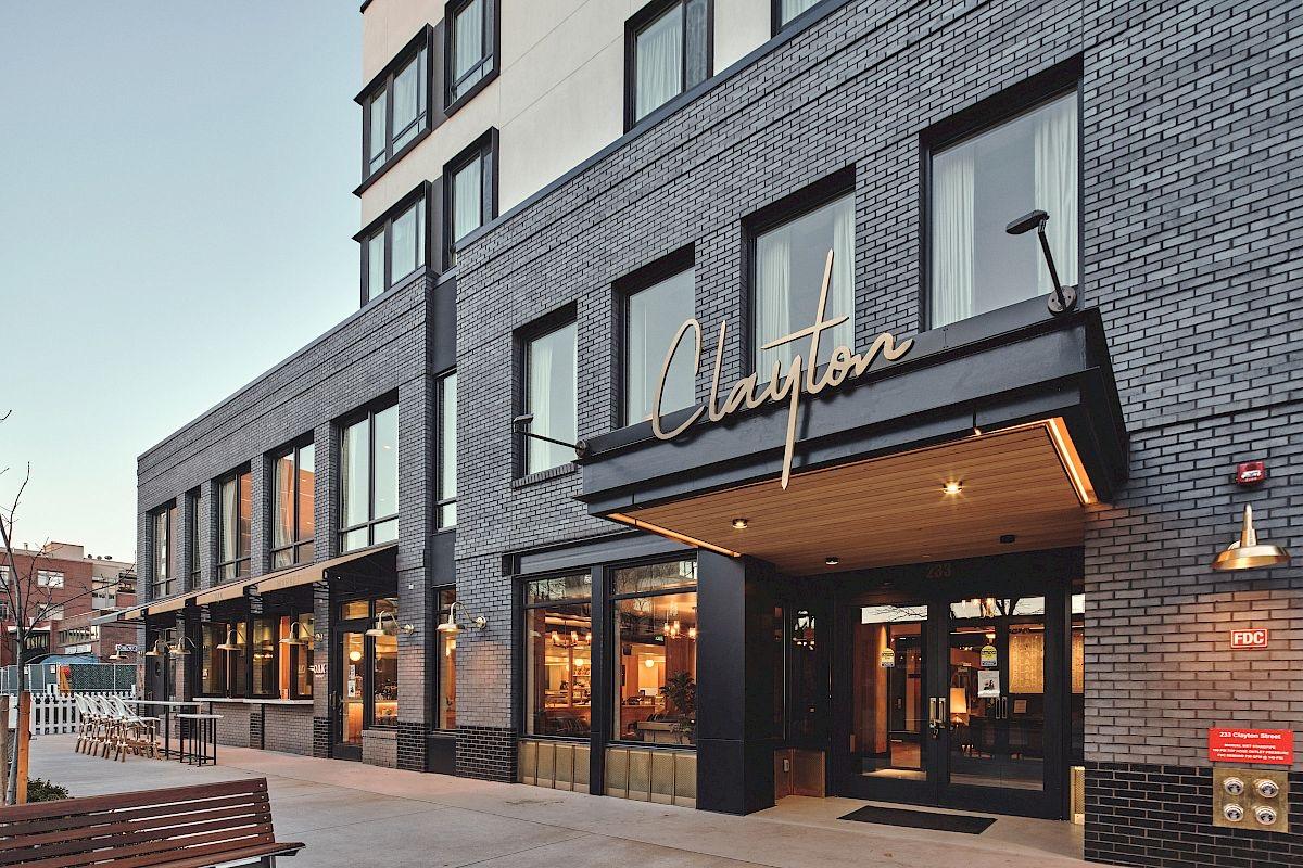 The hotel's dark brick front at dusk, its name in gold script above a lit wooden canopy over the entrance