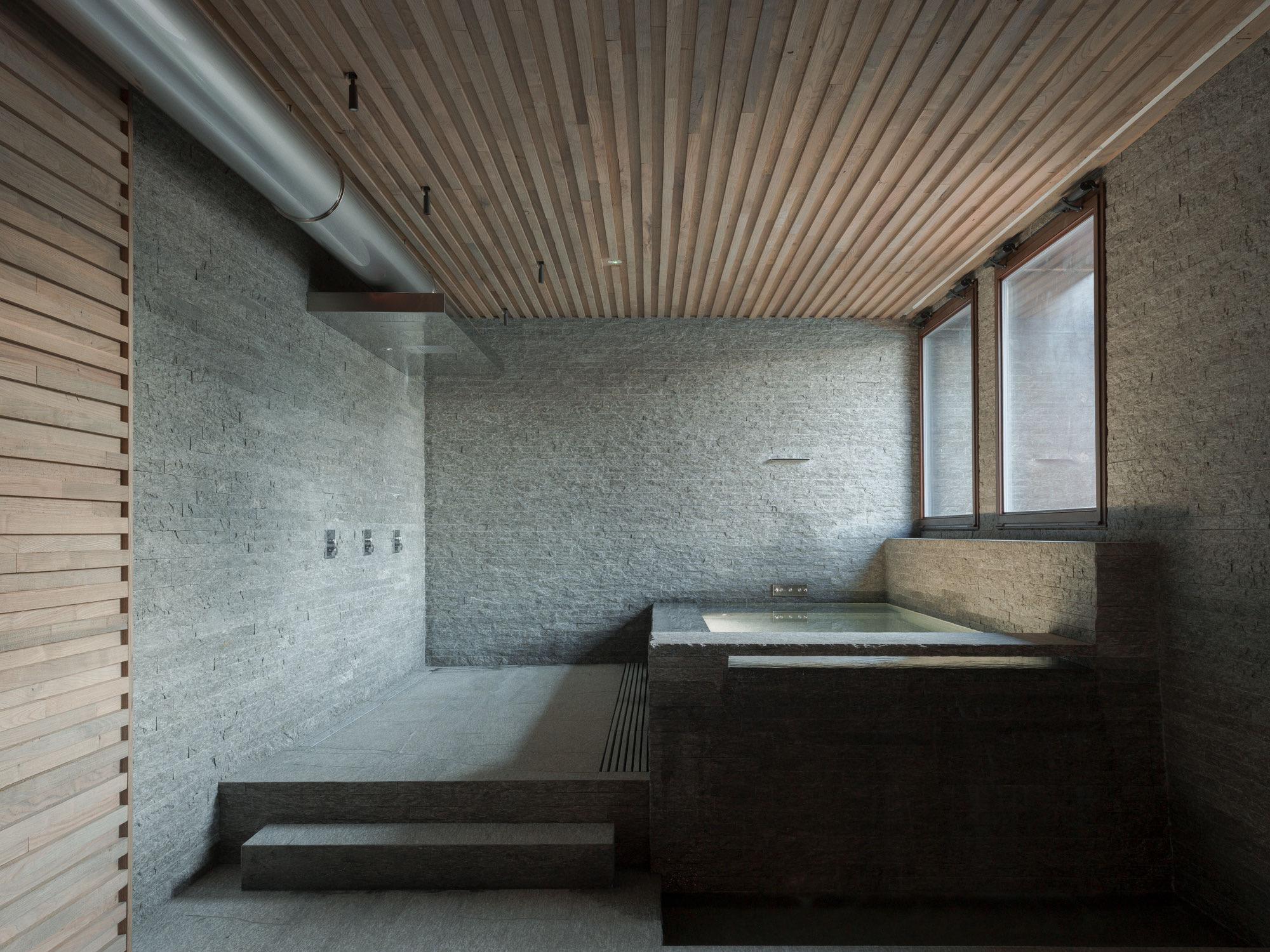 a stone wet room with a sunken tub, a wood slatted ceiling, and two windows