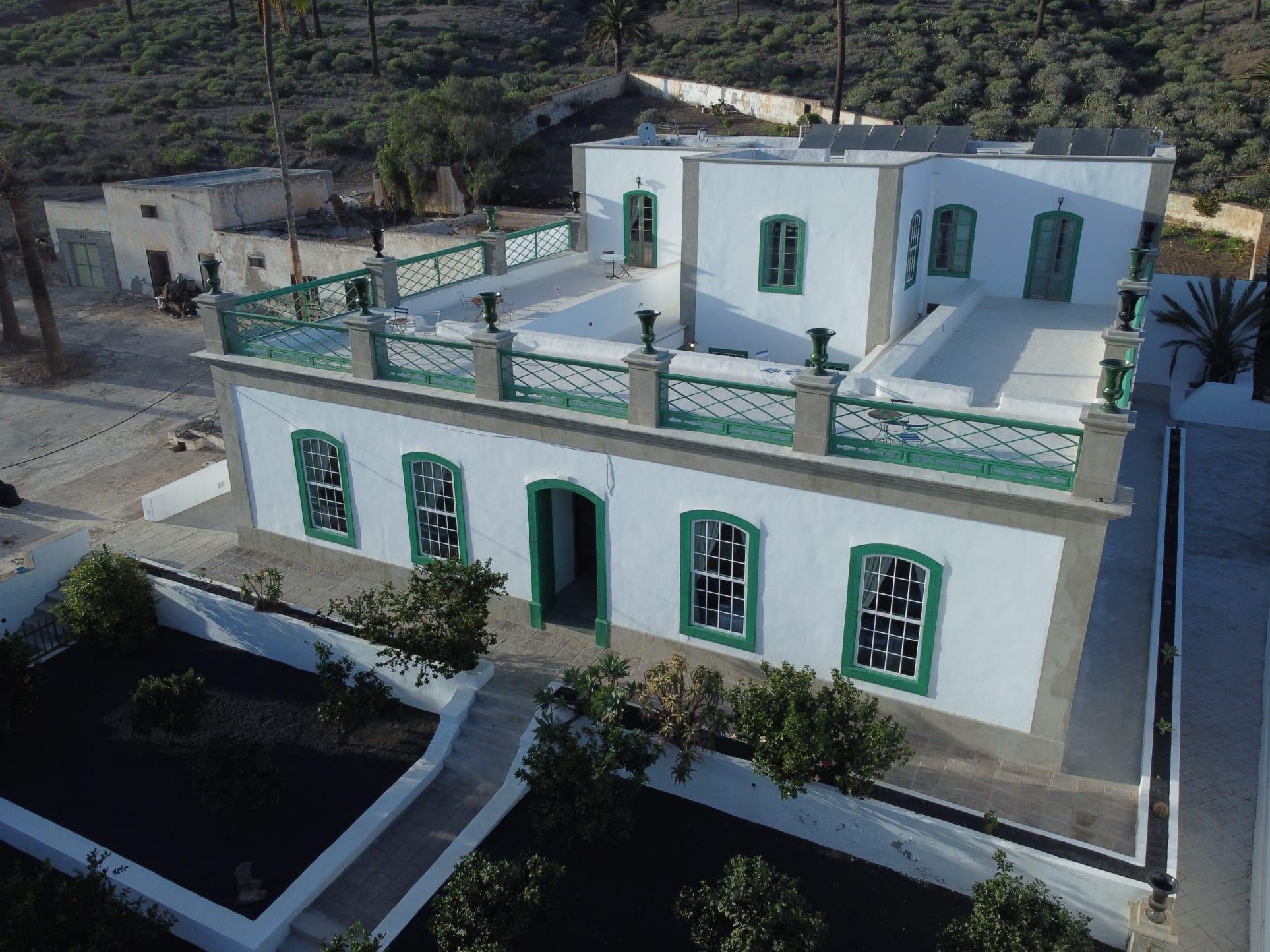 An aerial view of the whitewashed building with its green-railed roof terrace, surrounded by courtyards, outbuildings and scrubland.