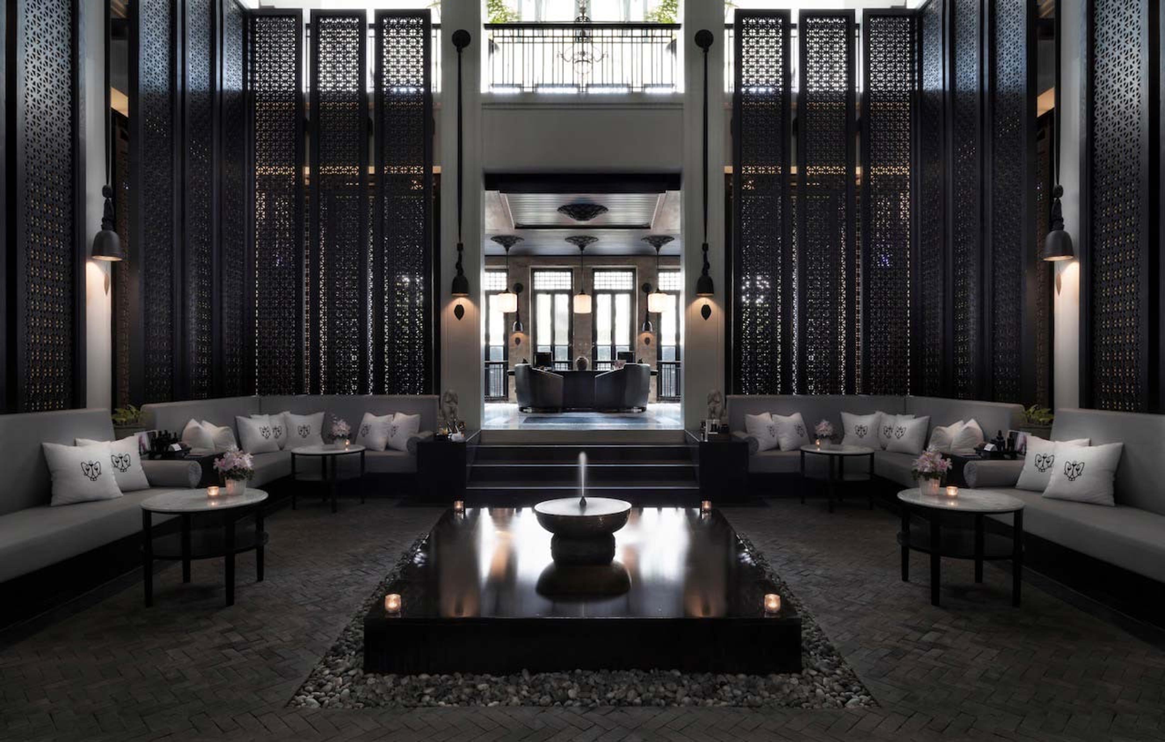 A dark screened entrance hall with a high ceiling, built-in sofas along both walls, and a small fountain set into a black stone floor.