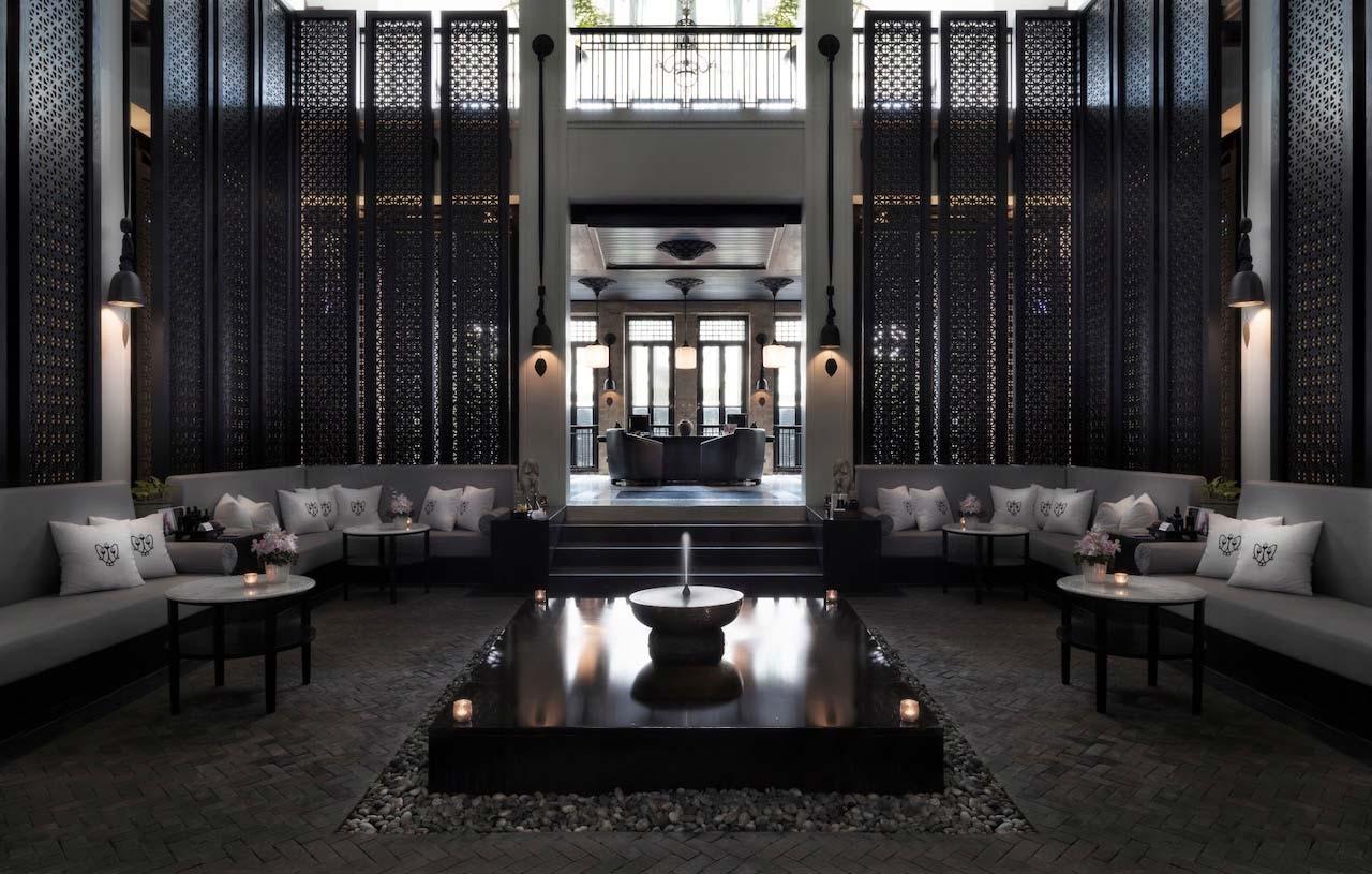 A dark screened entrance hall with a high ceiling, built-in sofas along both walls, and a small fountain set into a black stone floor.