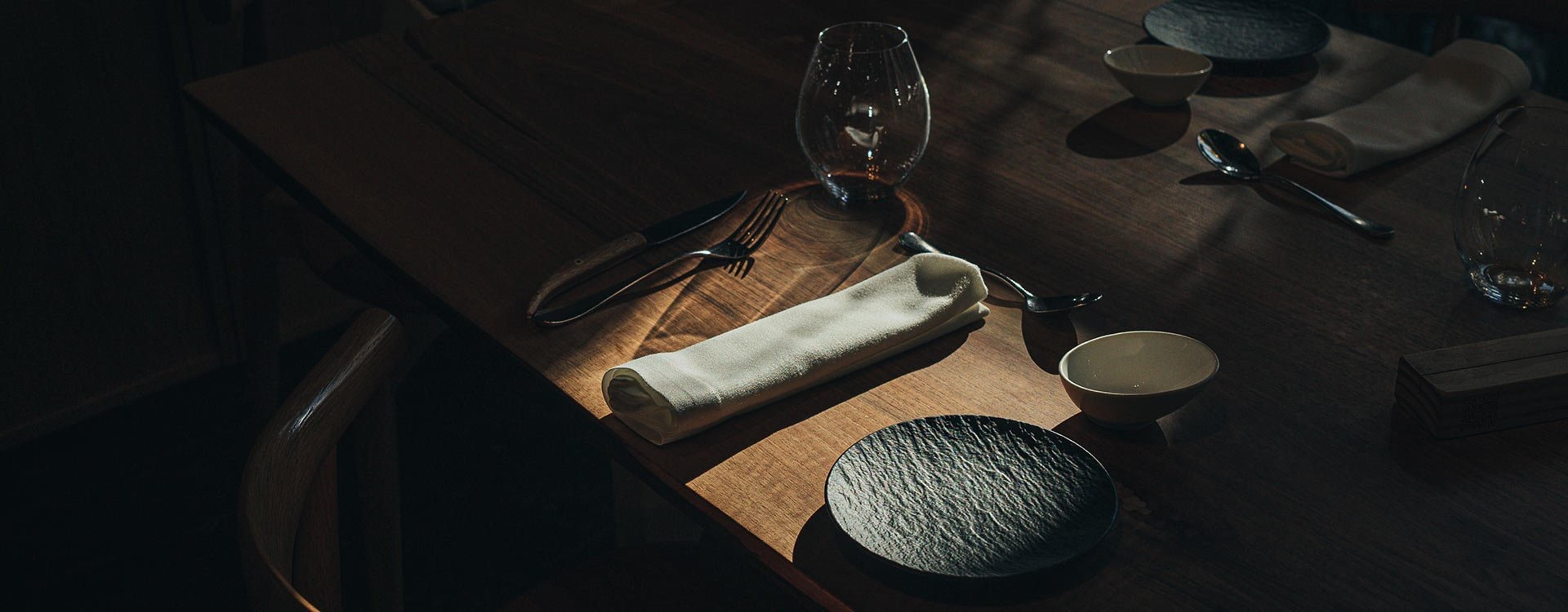 A laid table in Narru's dark dining room, a napkin and plate in a pool of light