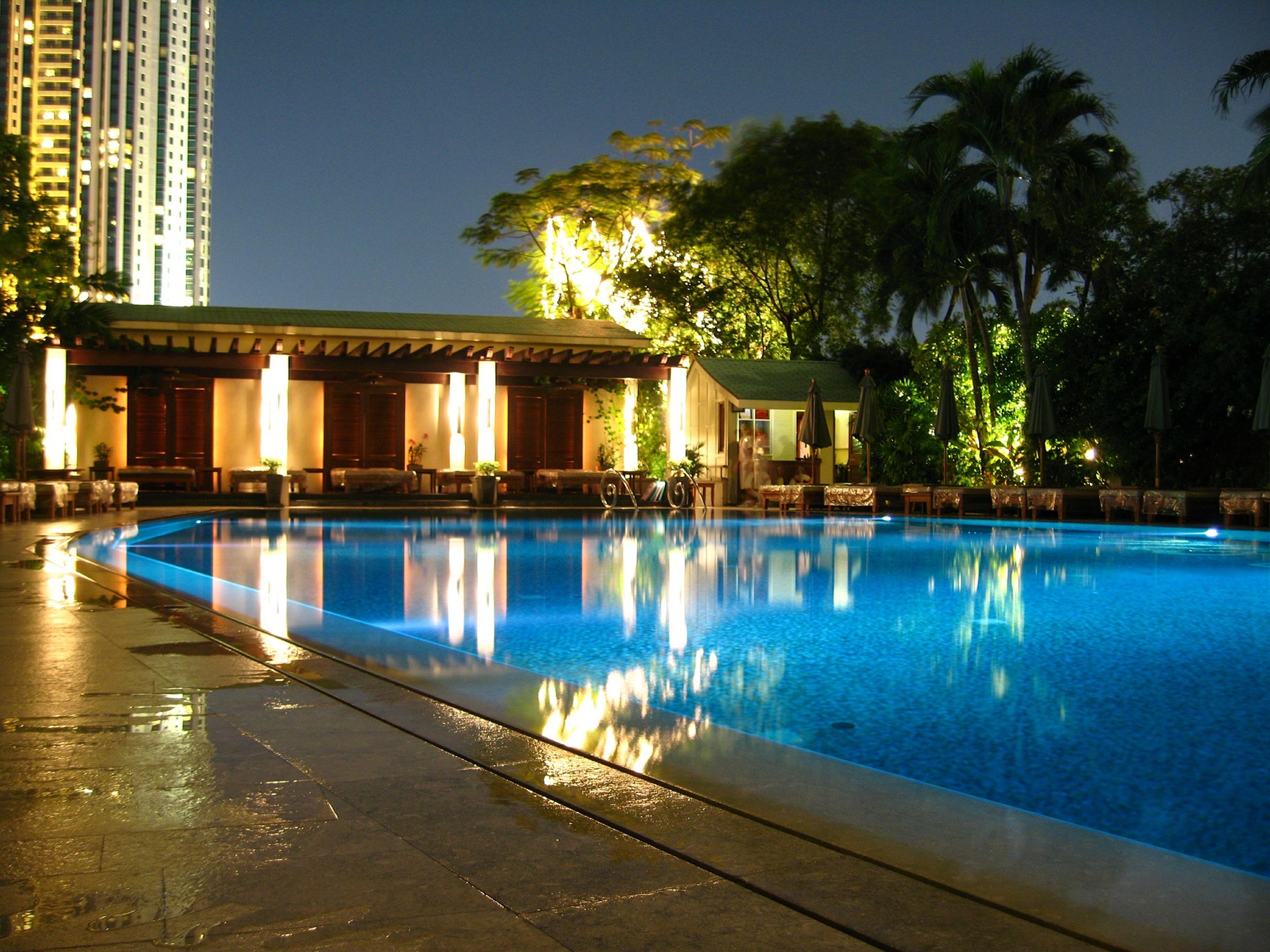 The hotel pool lit up at night beside a lantern-lit pavilion and palms