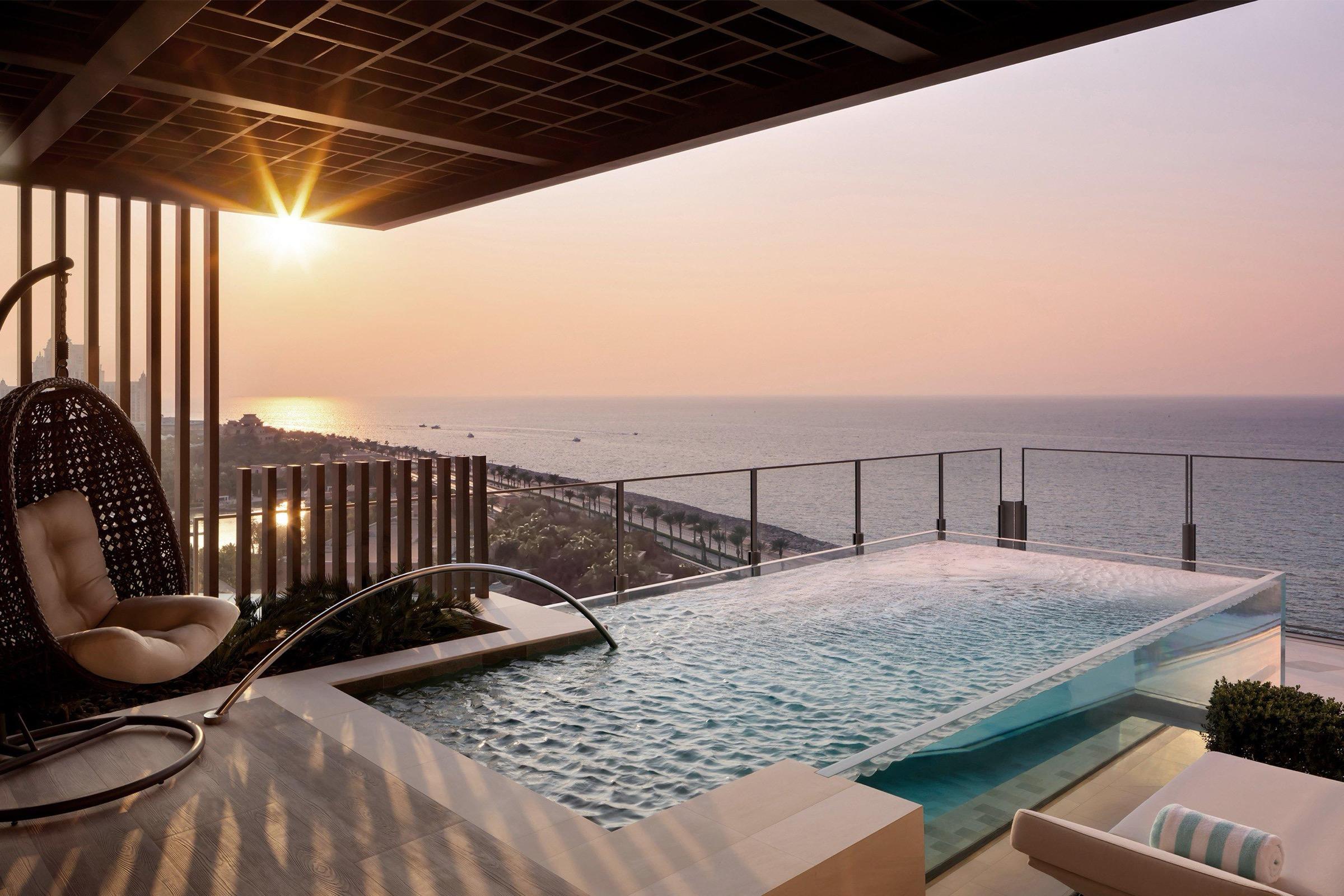 A glass-edged plunge pool and a hanging chair on a private terrace look out over the sea at sunset.