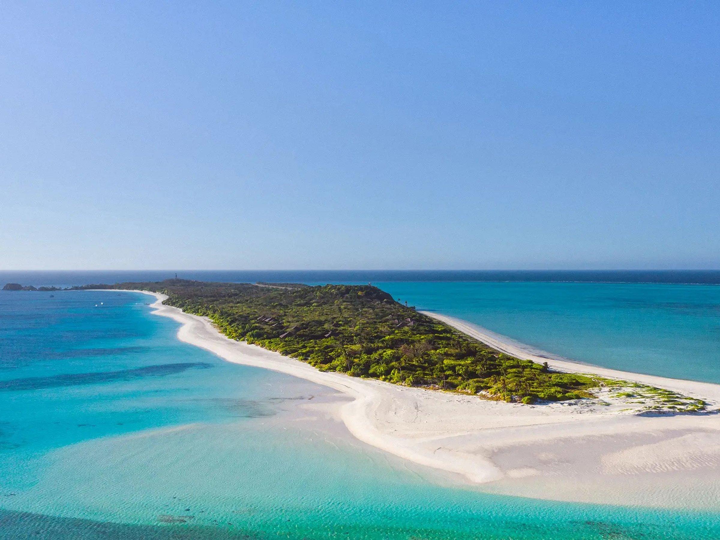 A long white sandbar curving out from a scrub-covered coral island into pale turquoise shallows in the Cuyo Islands