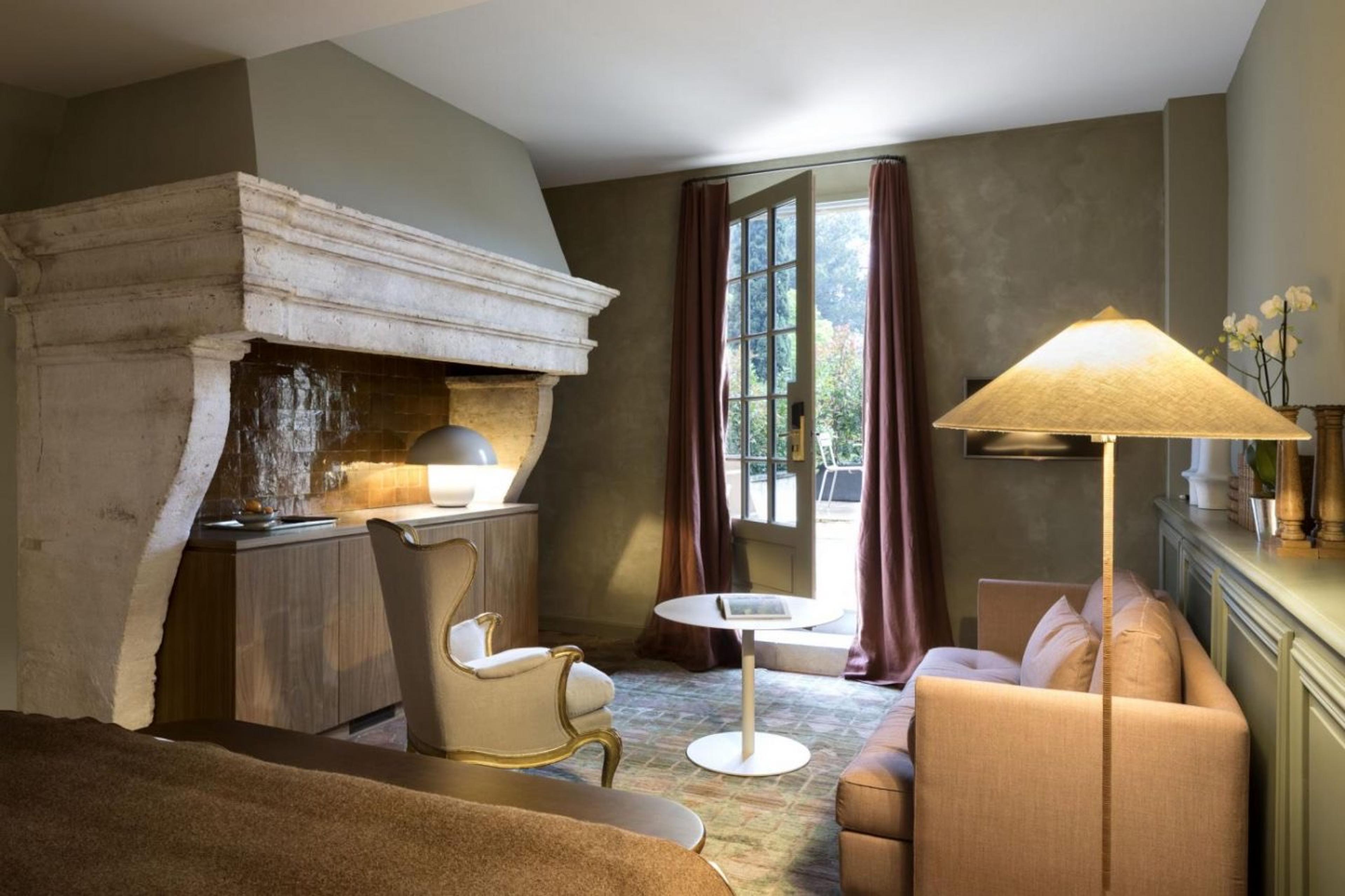 A sitting room with a carved stone fireplace hood, a gilt armchair and a sofa, with a door open to the garden.