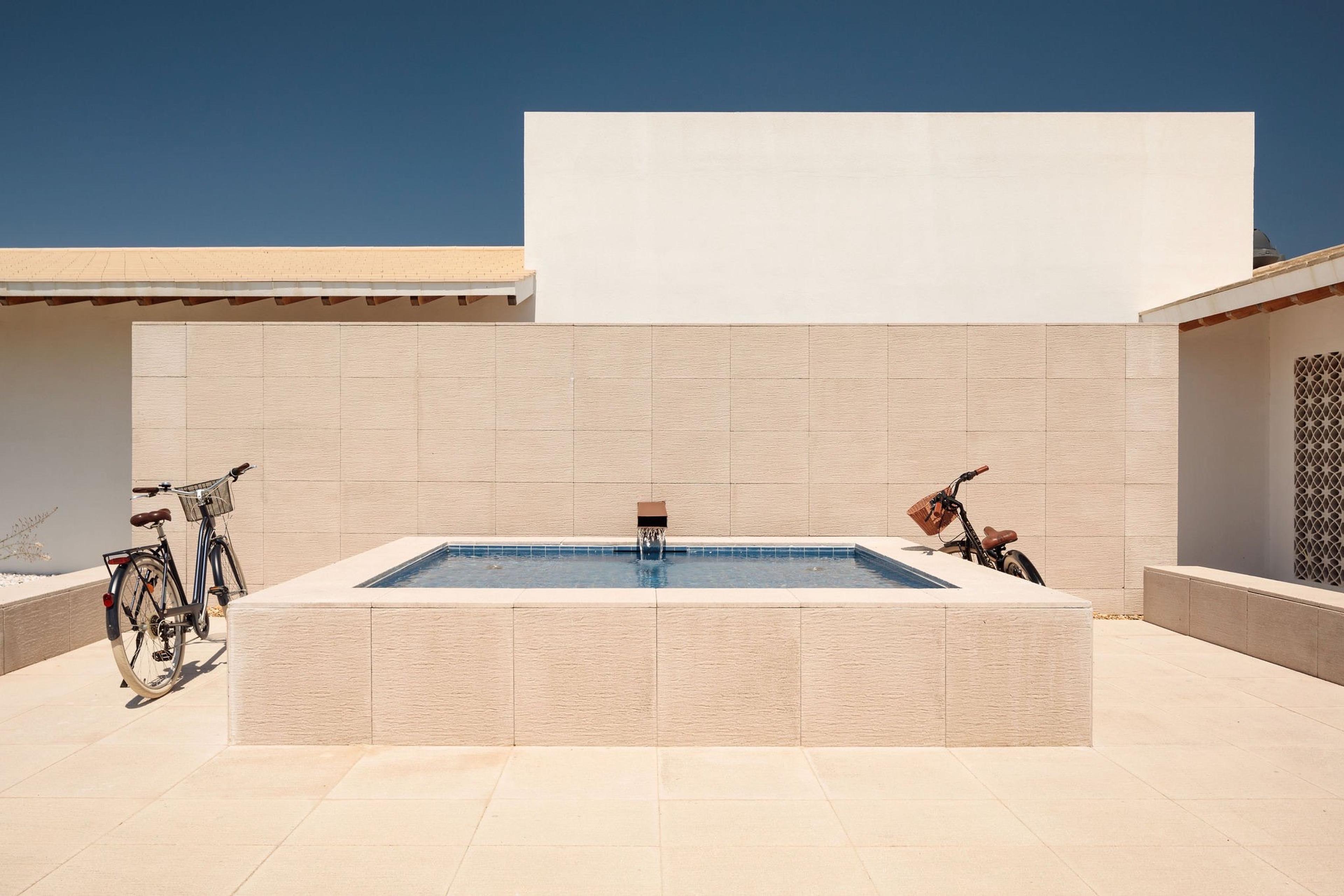 A small square plunge pool with two bicycles parked at its edge, tiled wall behind.