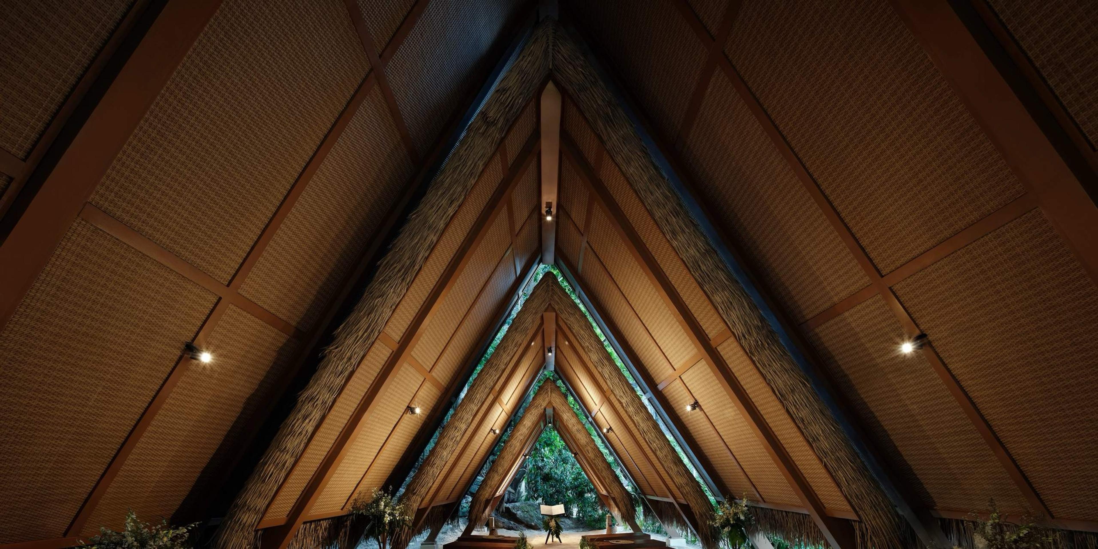 Looking up into a steep thatched roof lined in timber, light coming through at the peak.