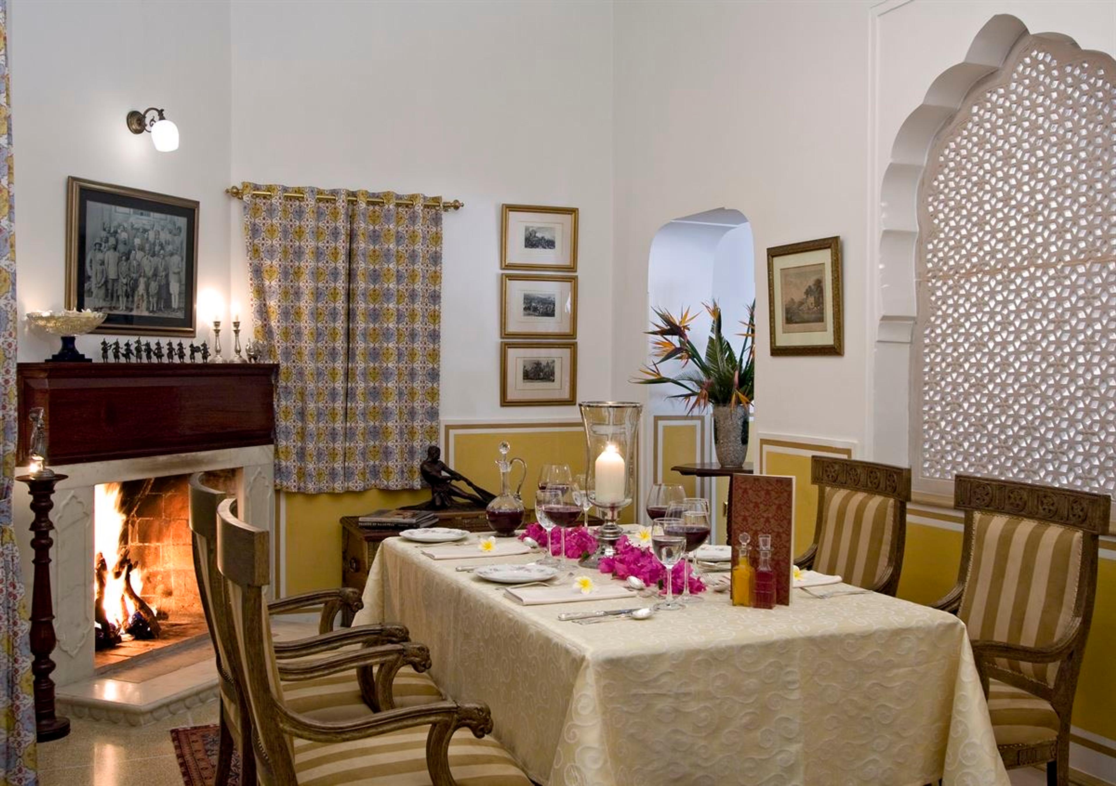 A small dining table set for two with wine glasses and flowers in front of a lit fireplace.