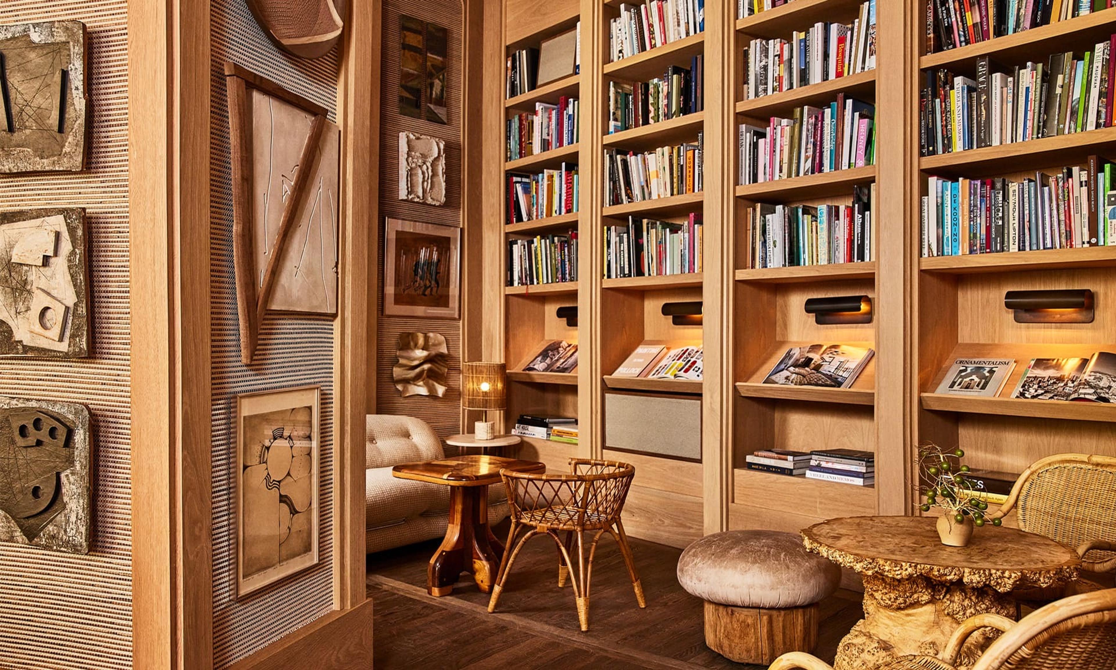 A reading nook lined with bookshelves beside a tiled wall hung with abstract wooden artworks, with a rattan chair and ottoman.