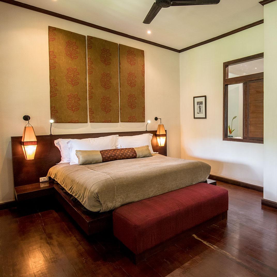 A bedroom in dark wood with a red bench at the foot of the bed