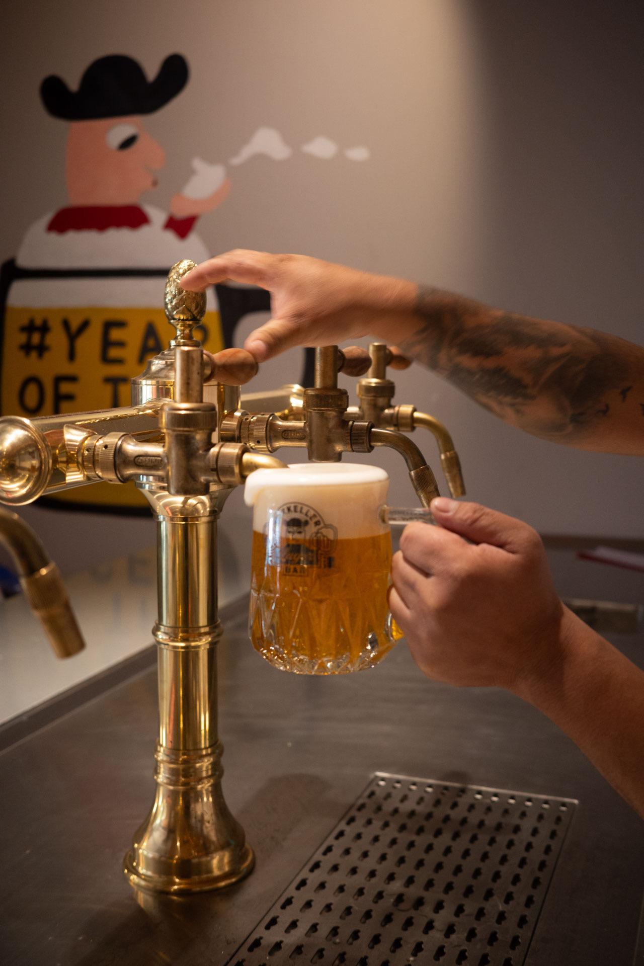 A Mikkeller beer being poured from a brass tap into a dimpled glass mug