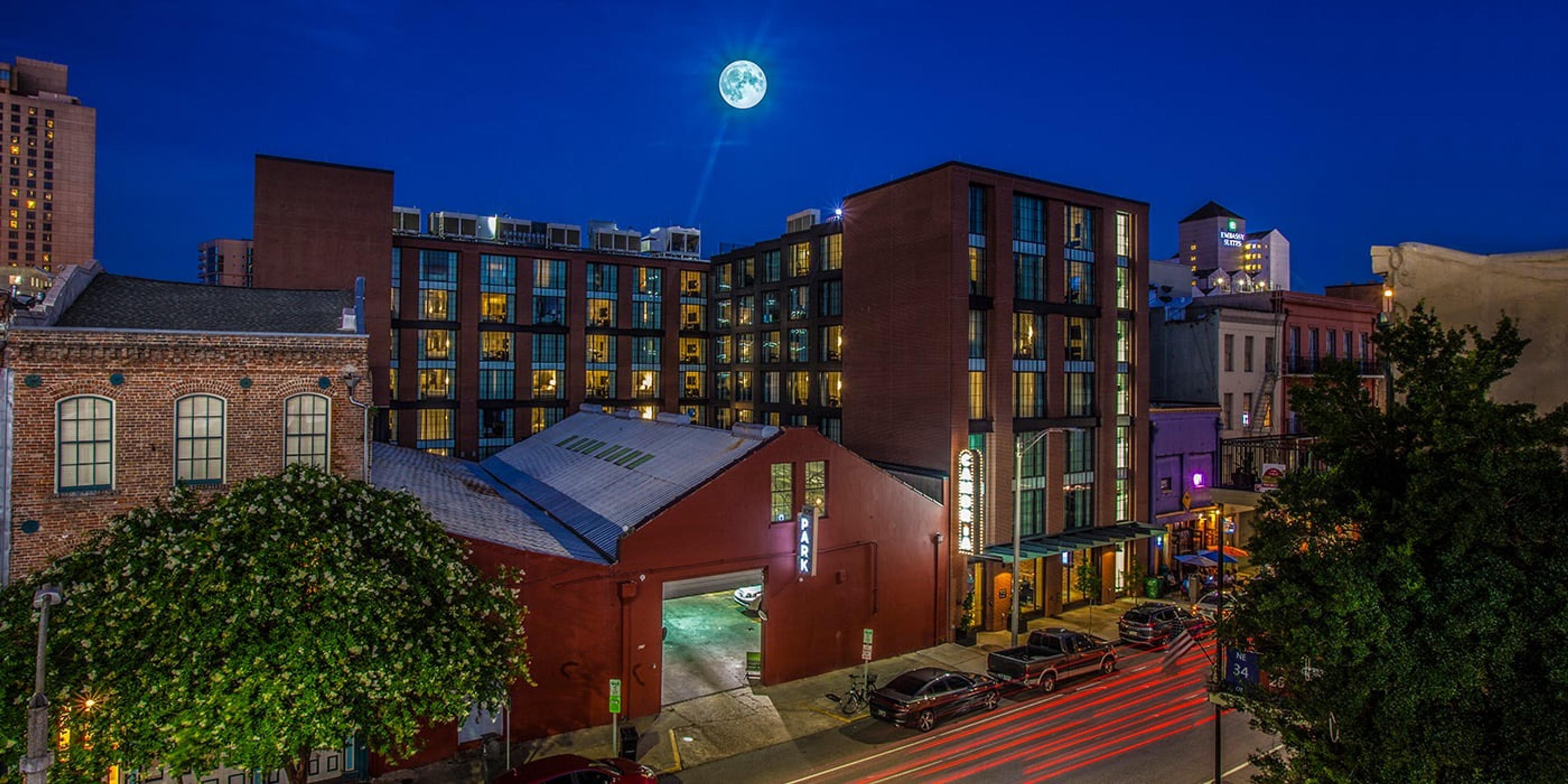 A brick hotel building lit up at night under a full moon, with light trails from passing cars on the street below.