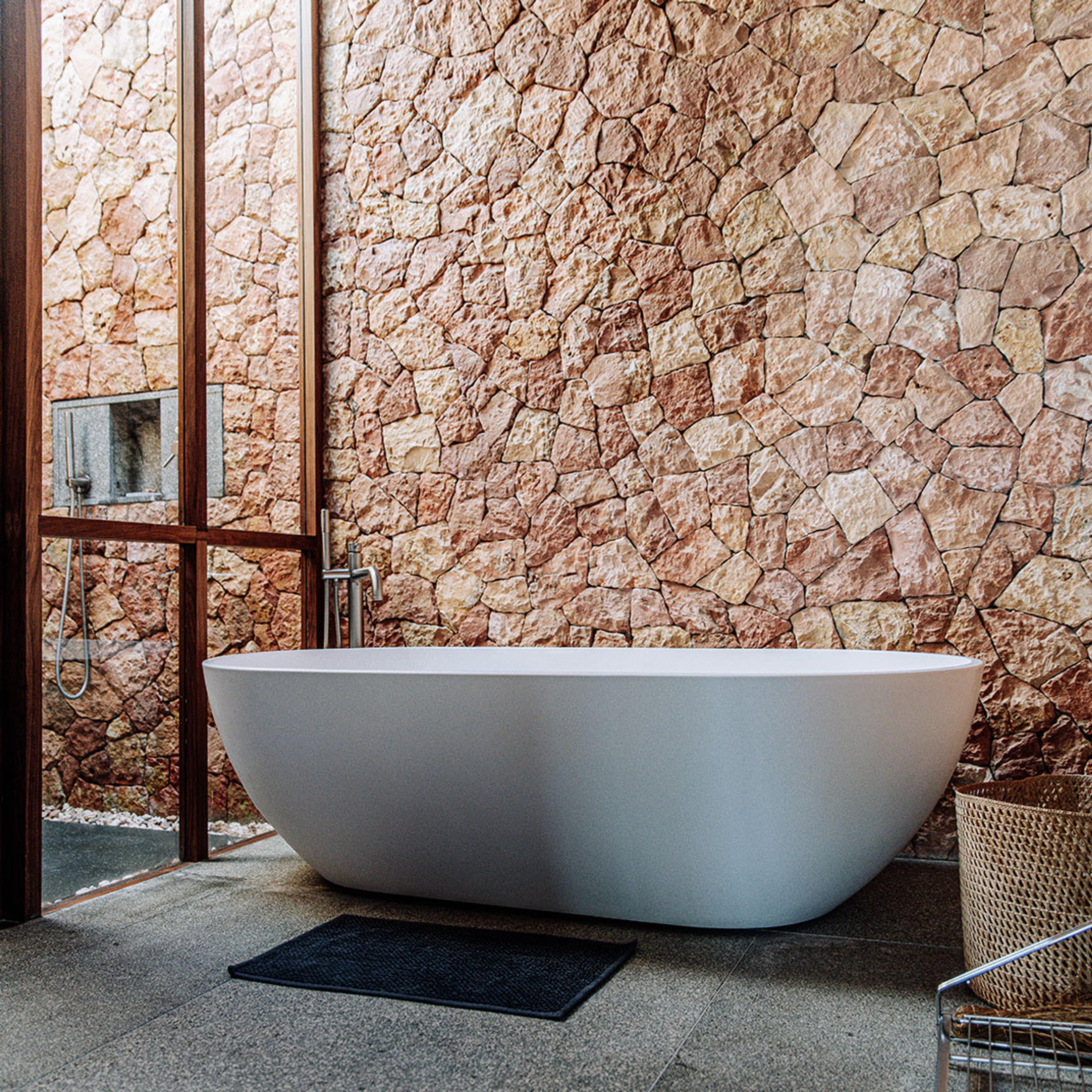 A freestanding bath against a coral-stone wall