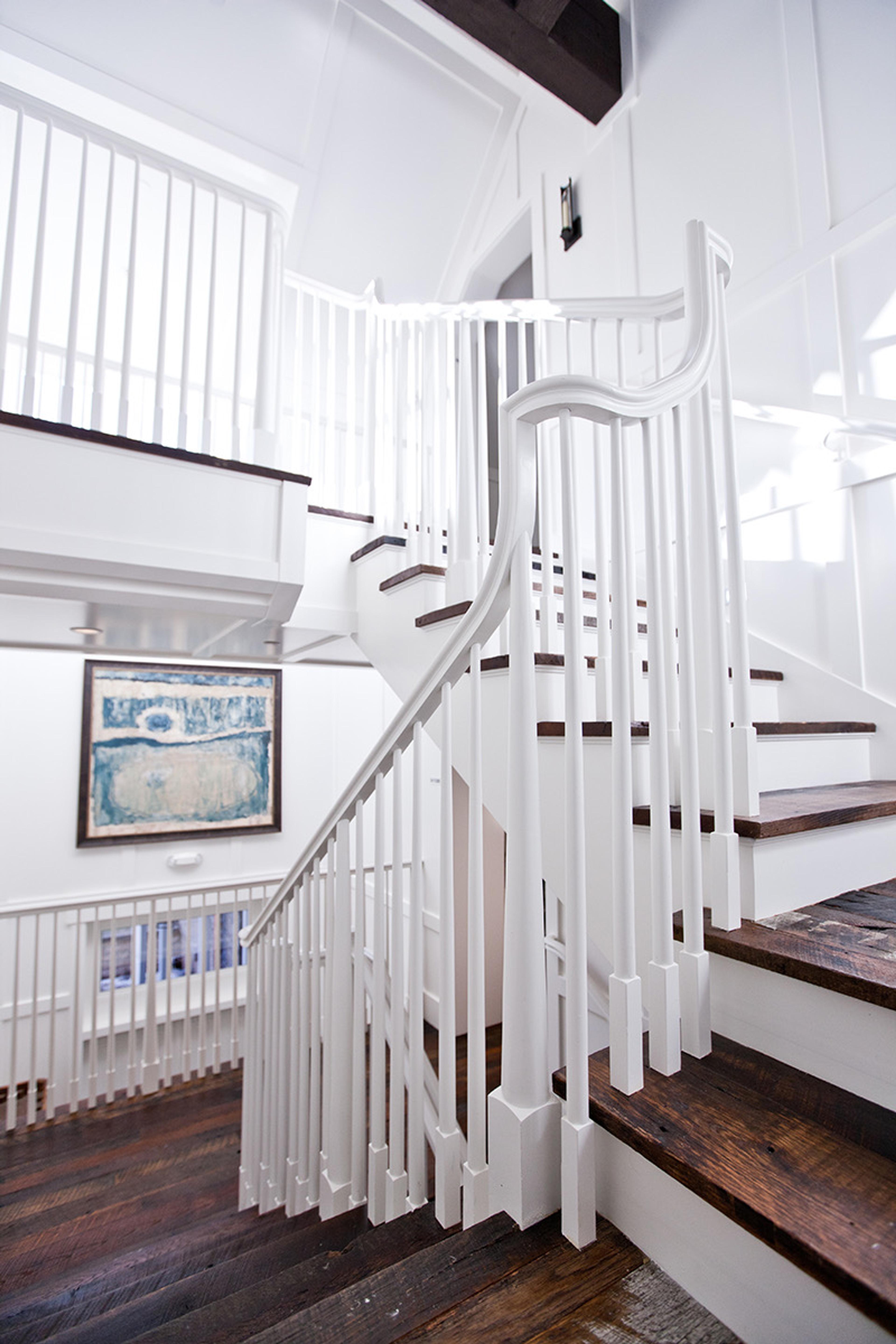 A white painted staircase with dark wood treads curving down past a framed picture on the wall.