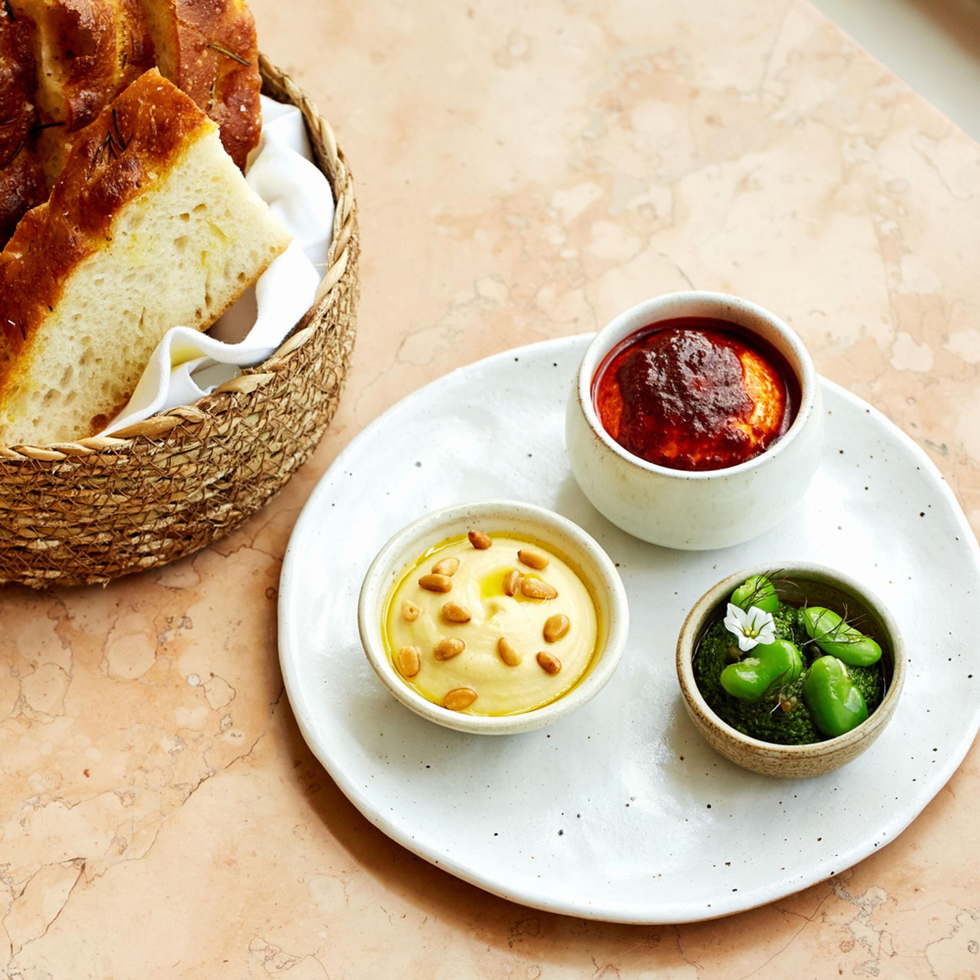 Sharing plates of bread, dips and broad beans on a pale table