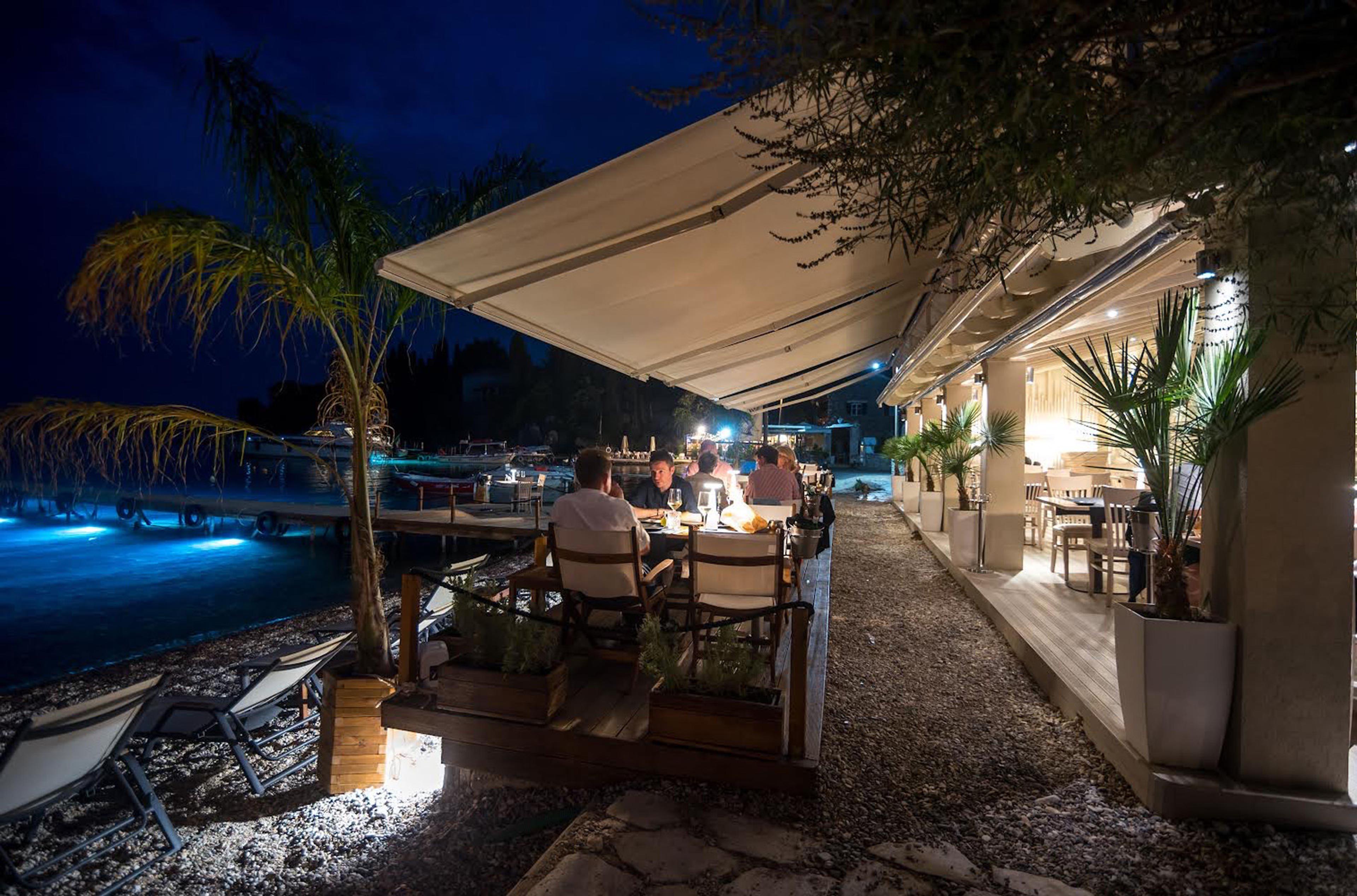 Tables under a canopy beside the water at night, the bay lit blue below