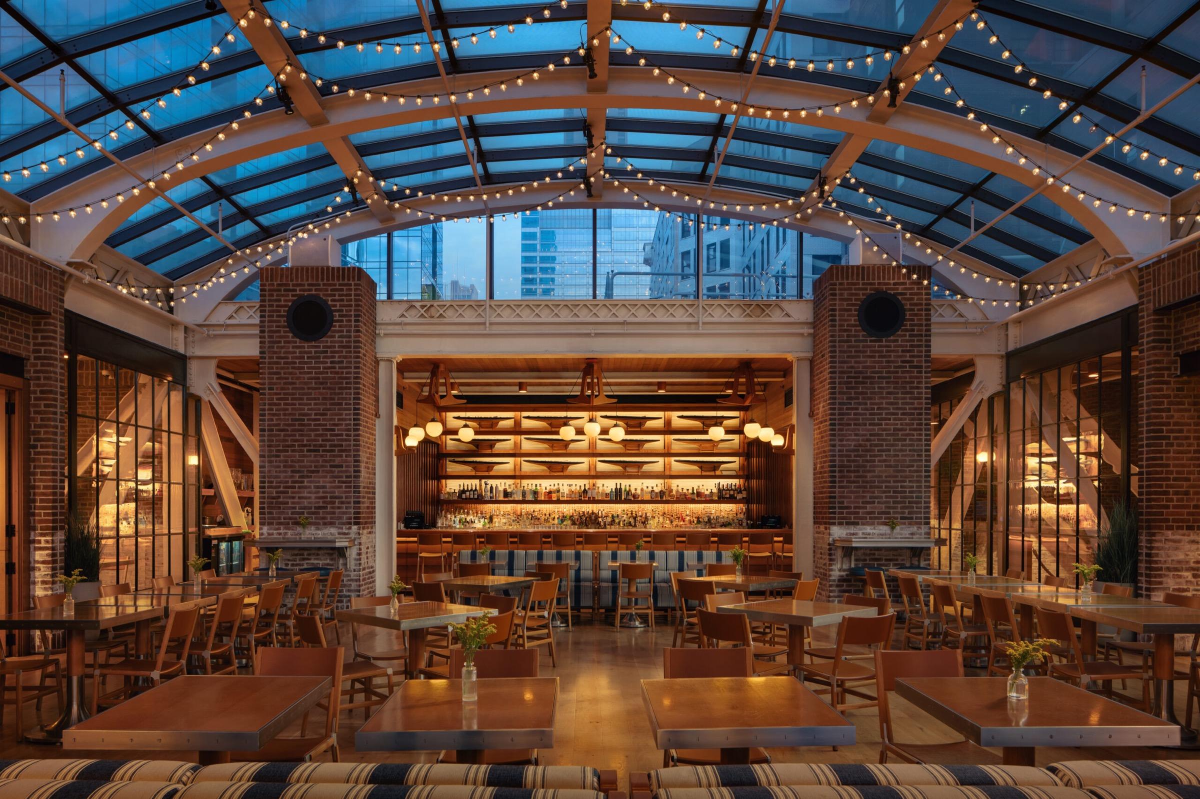Cindy's, the rooftop restaurant, under its arched glass roof at dusk, strung with lights above long wooden tables and a bar