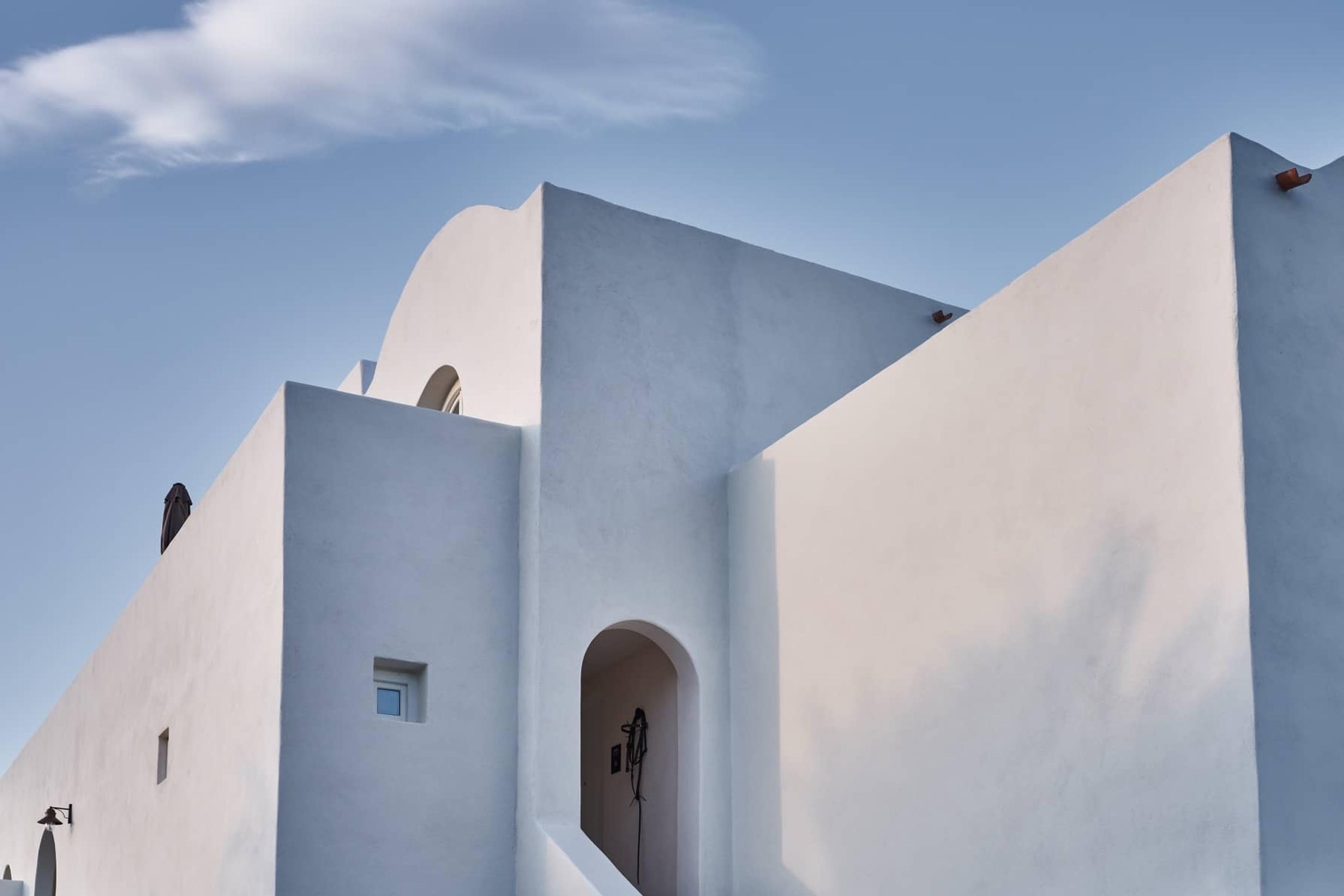 The white stepped corner of a Cycladic building against a clear blue sky.