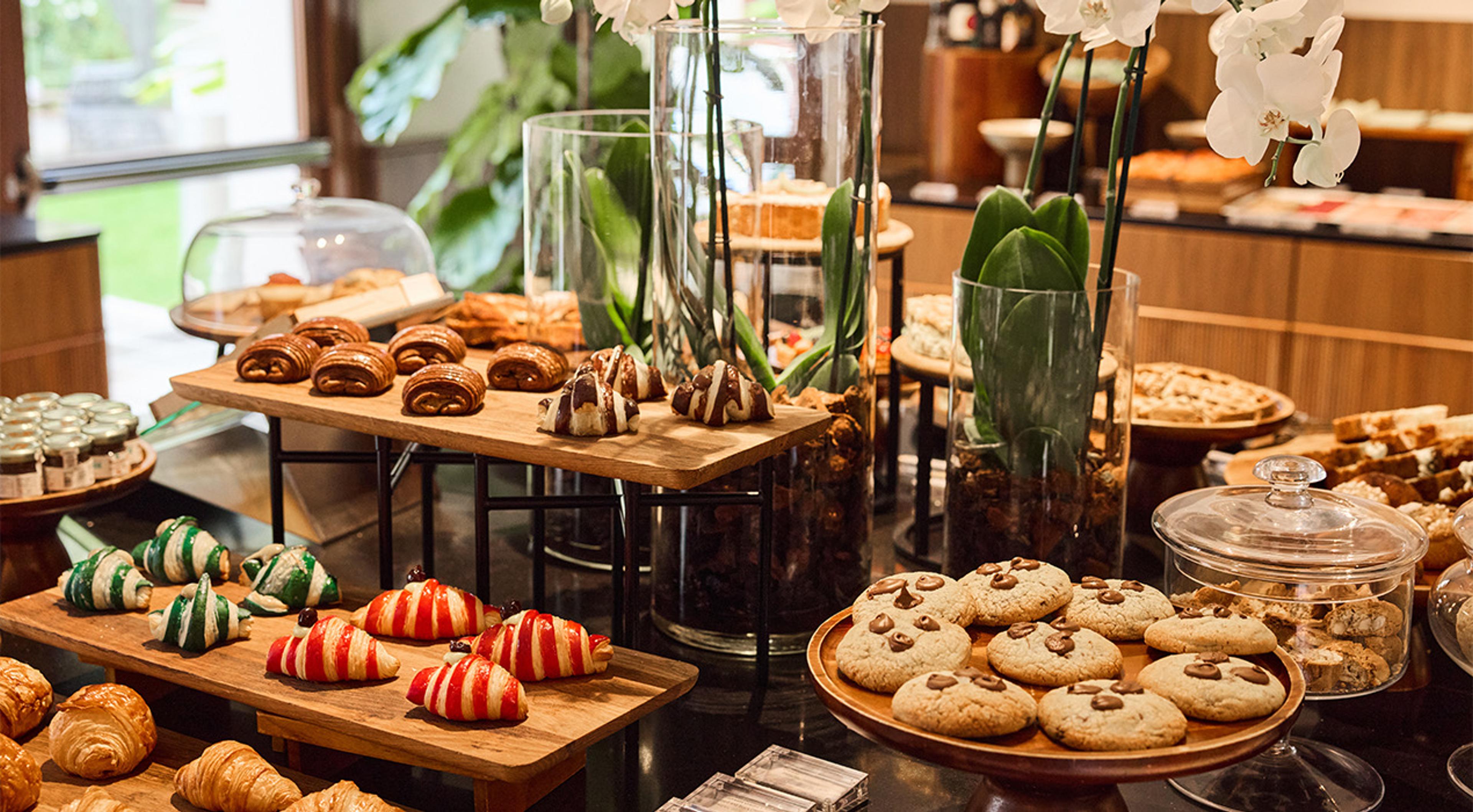 A buffet table of pastries, cookies and jams, with orchids in glass vases and a view to a garden behind.
