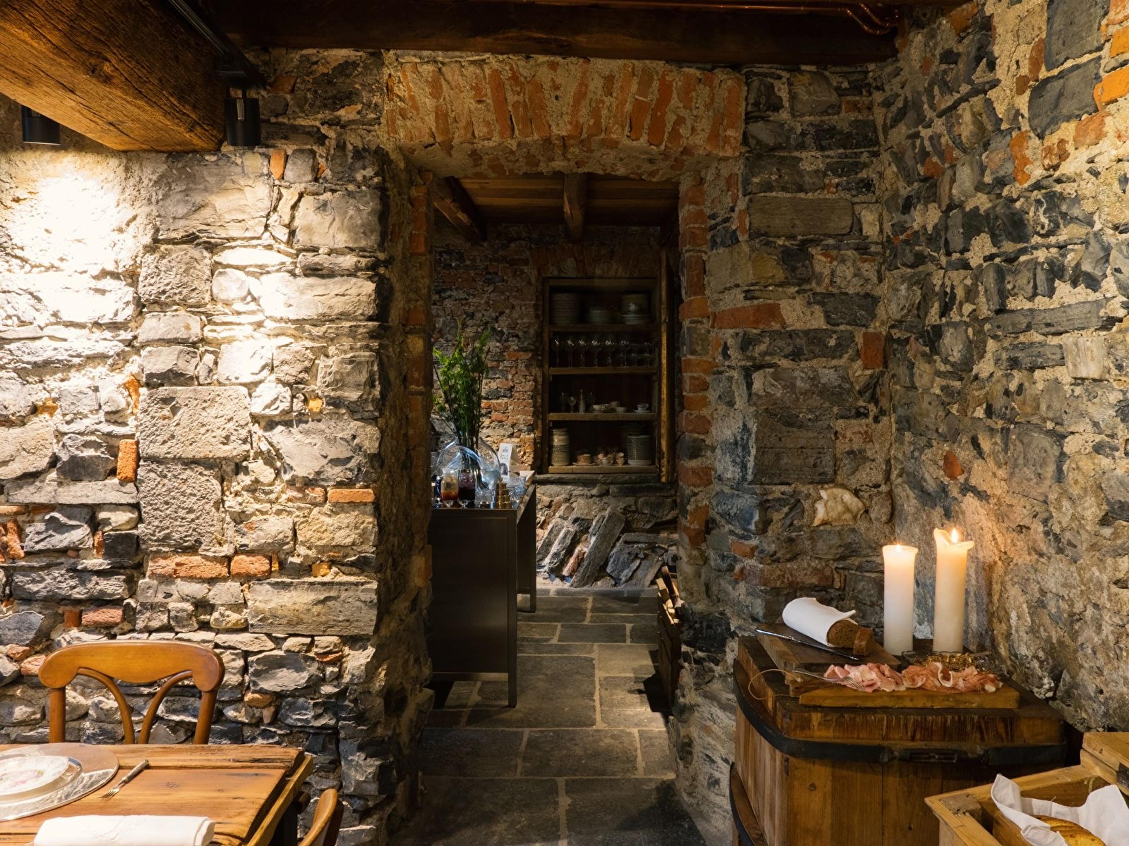 a stone-walled corridor leading to a pantry, with a charcuterie board and lit candles resting on a barrel in the foreground